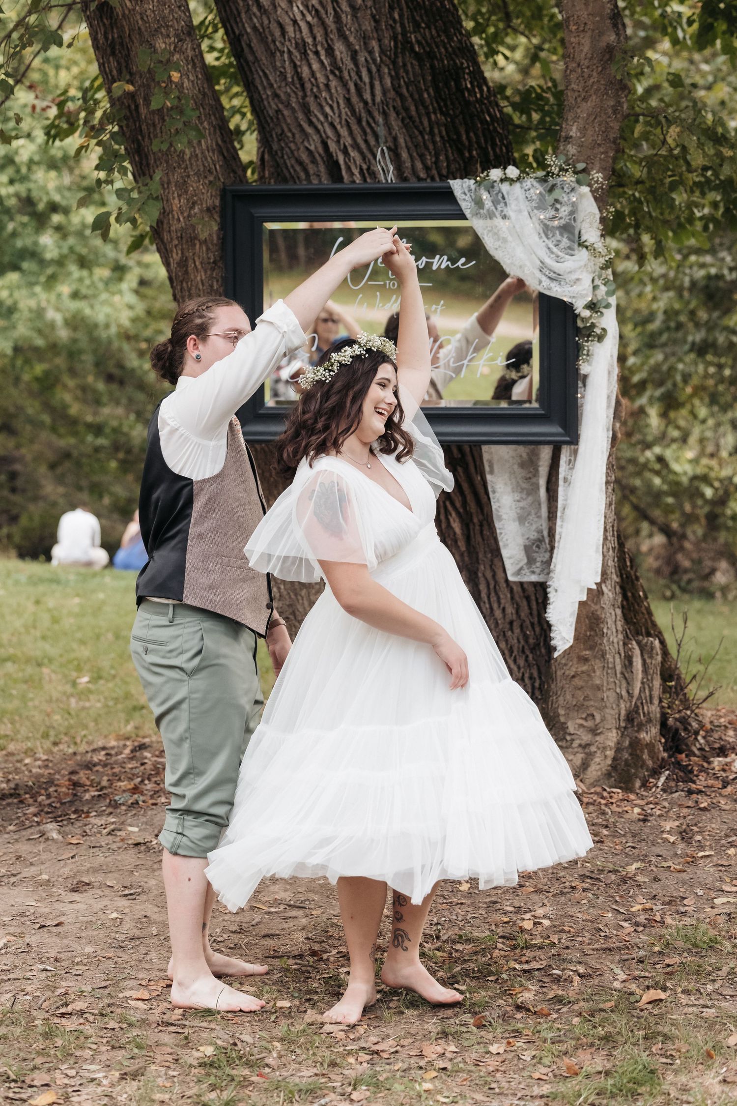 Couple dances playfully under trees during outdoor wedding celebration.