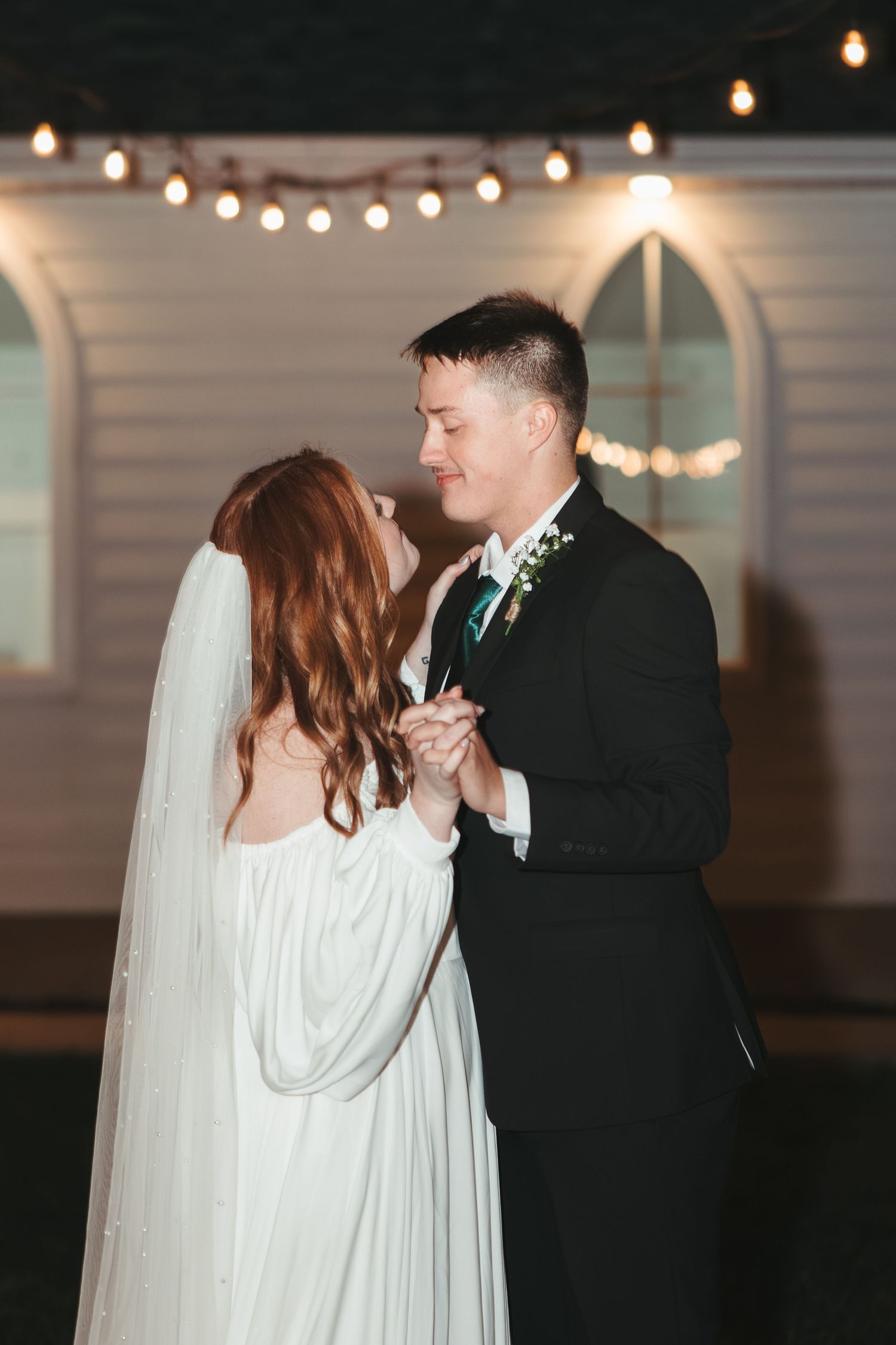 A couple sharing an intimate dance moment under string lights at their wedding.