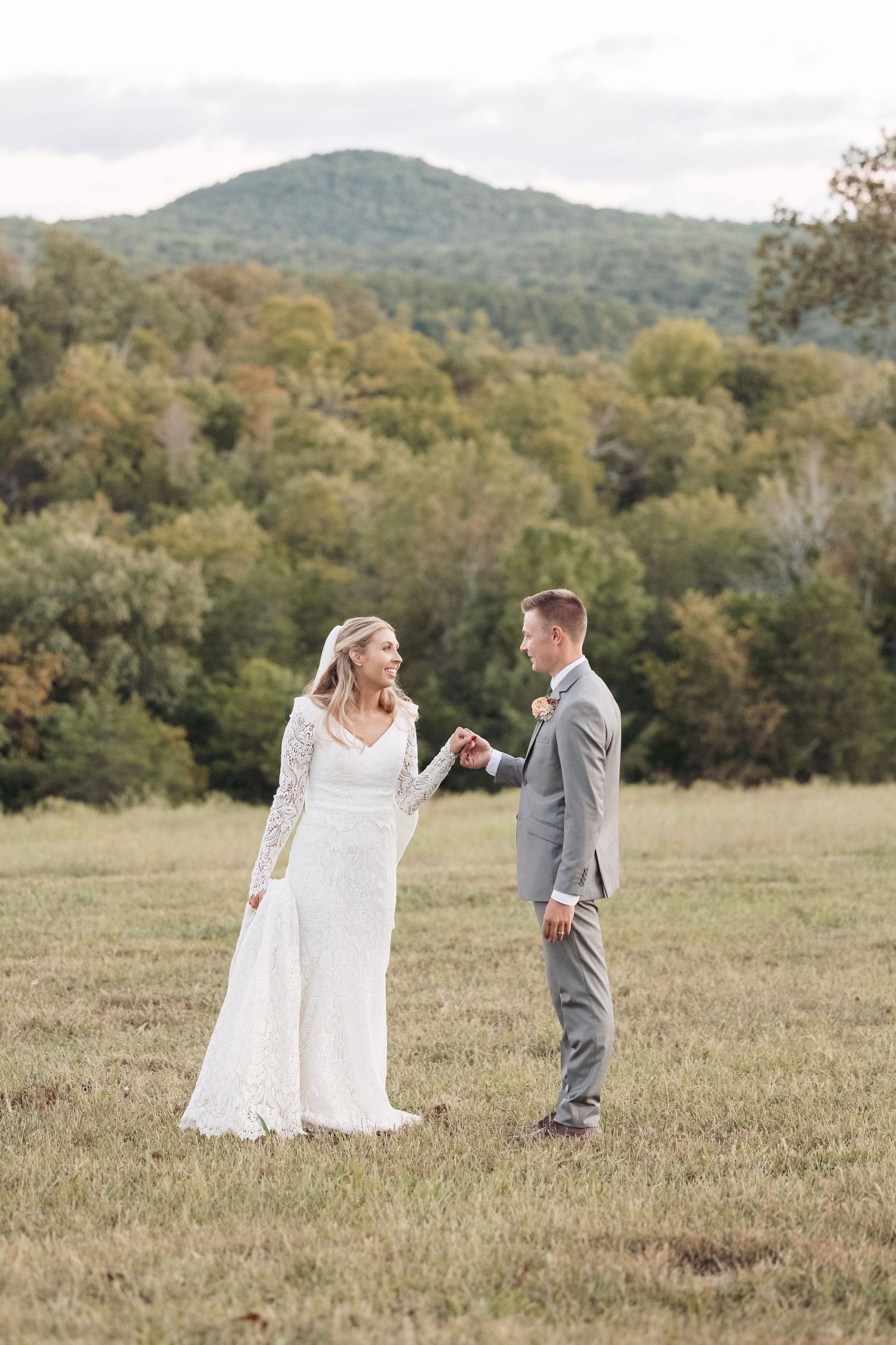 Romantic wedding couple sharing a moment in field with mountain backdrop.