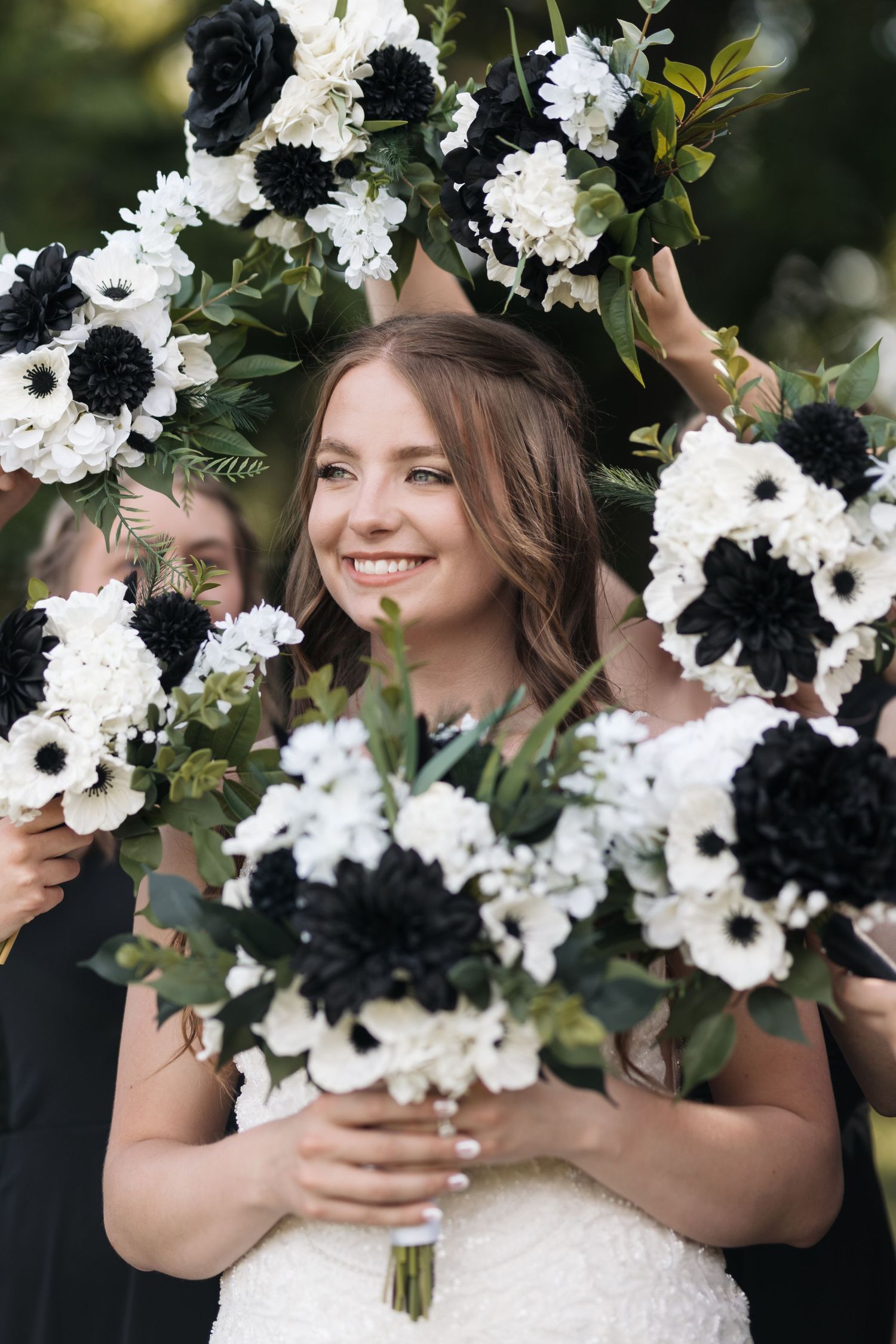 Wedding bouquets featuring striking black and white flowers frame a beautiful bridal portrait.