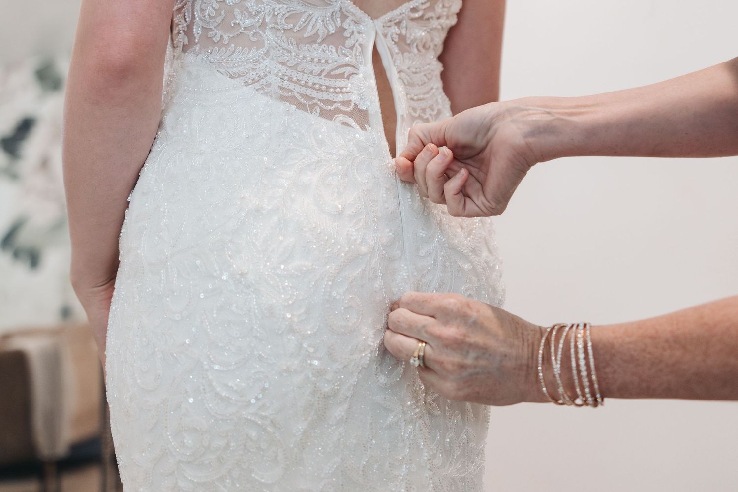 Close-up of hands fastening delicate lace buttons on a white wedding dress.