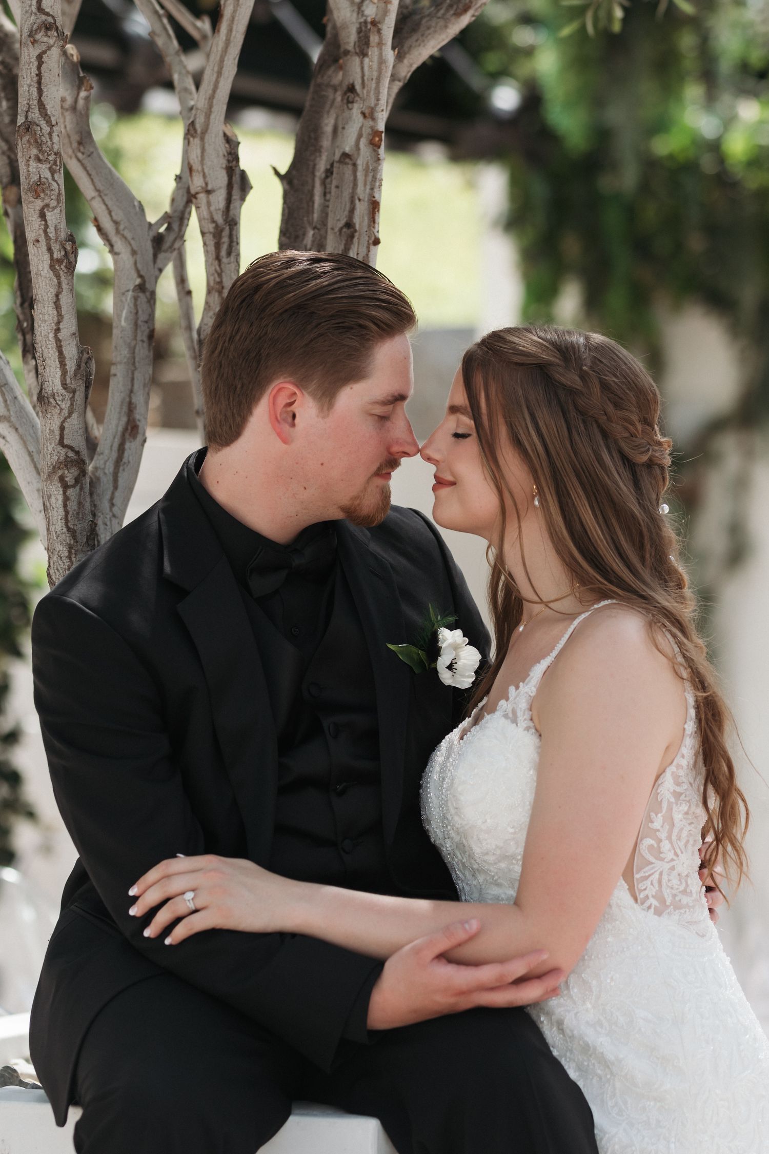 Wedding couple sharing an intimate moment while sitting among bare branches and greenery.