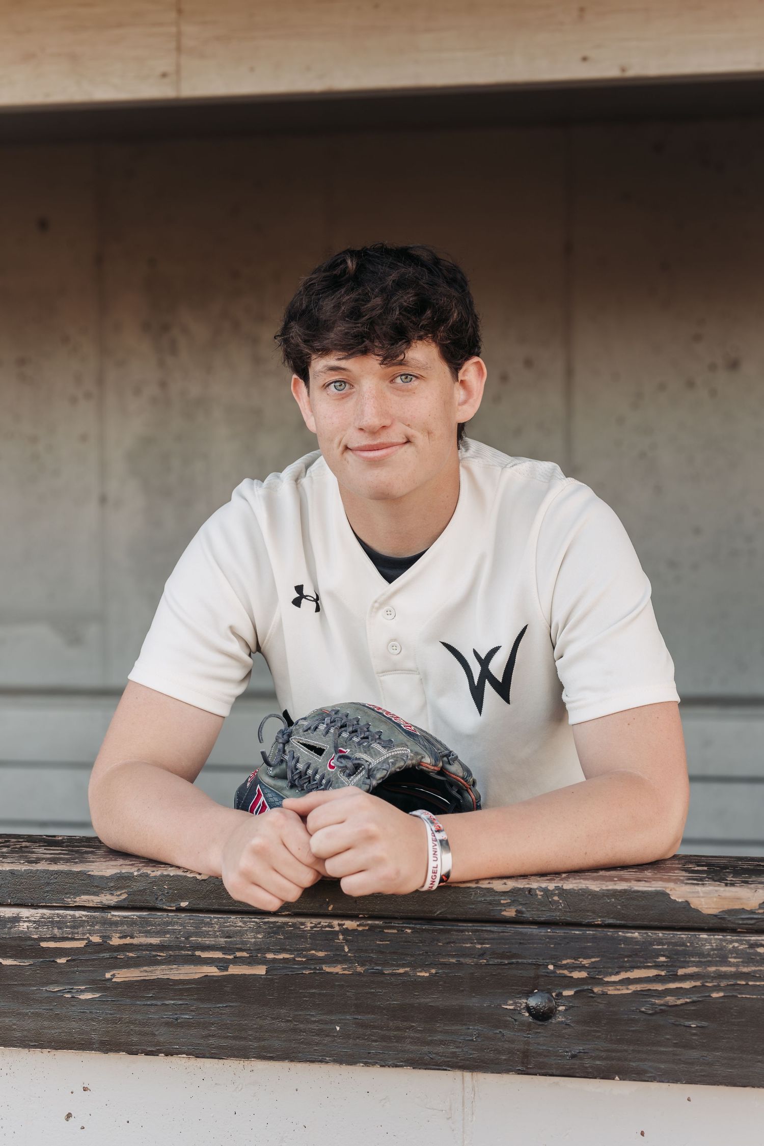 Baseball player in white Under Armour jersey posing with glove in dugout.