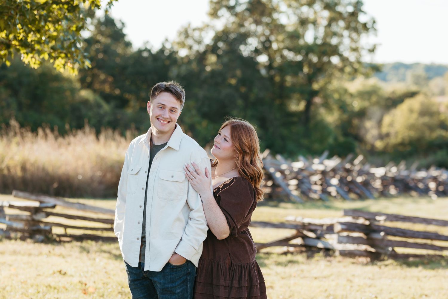 Playful couple enjoying autumn afternoon by wooden split-rail fence.