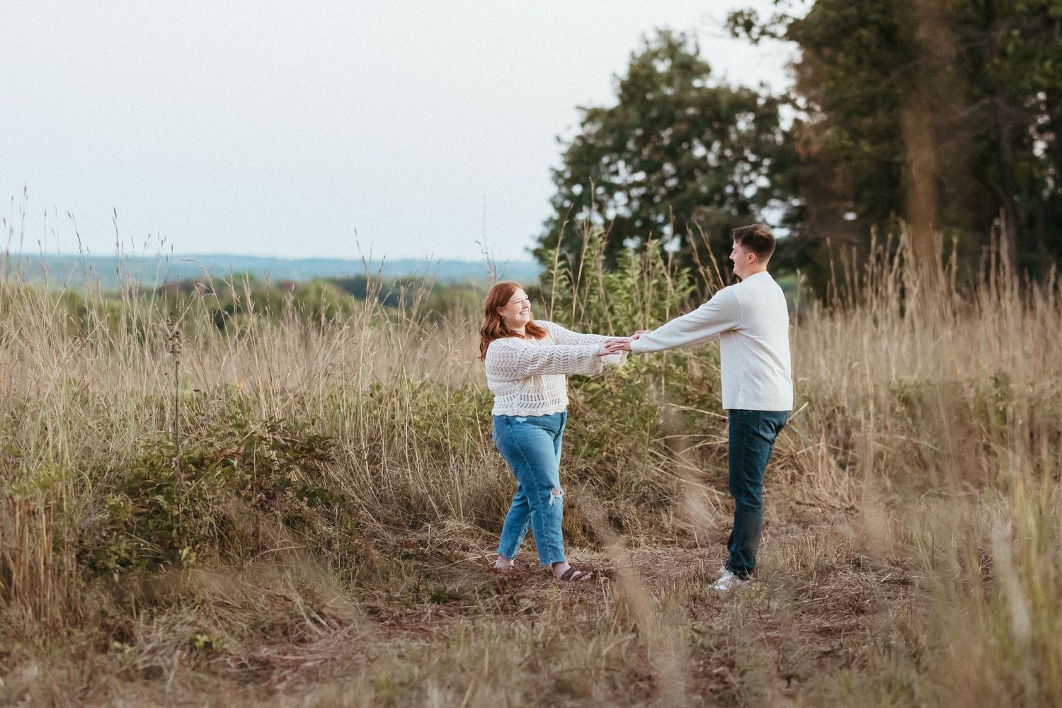 Two people dance and twirl together in a rustic field with mountains in the distance.