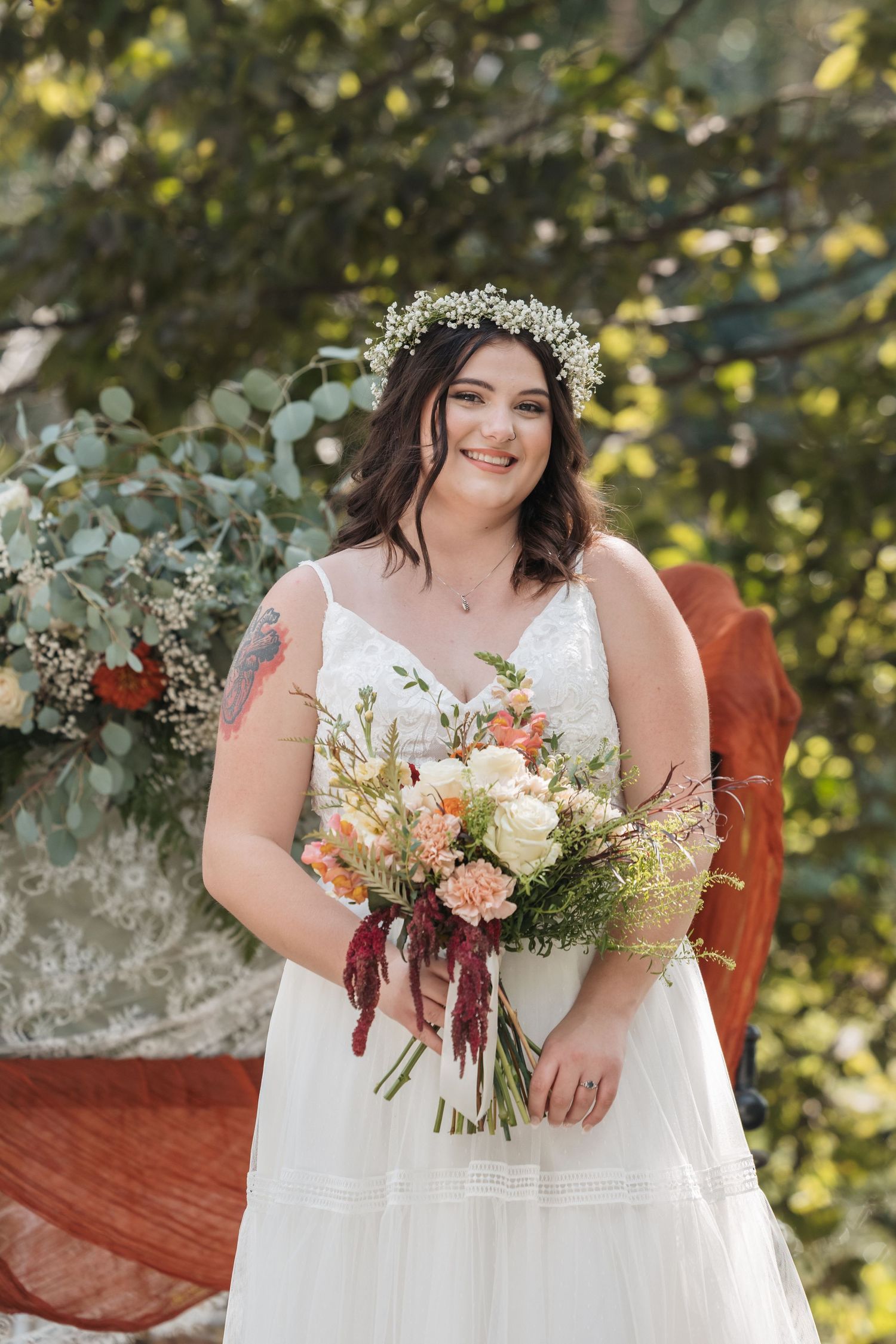 Bride in plus size gown holding autumn bouquet against natural backdrop.