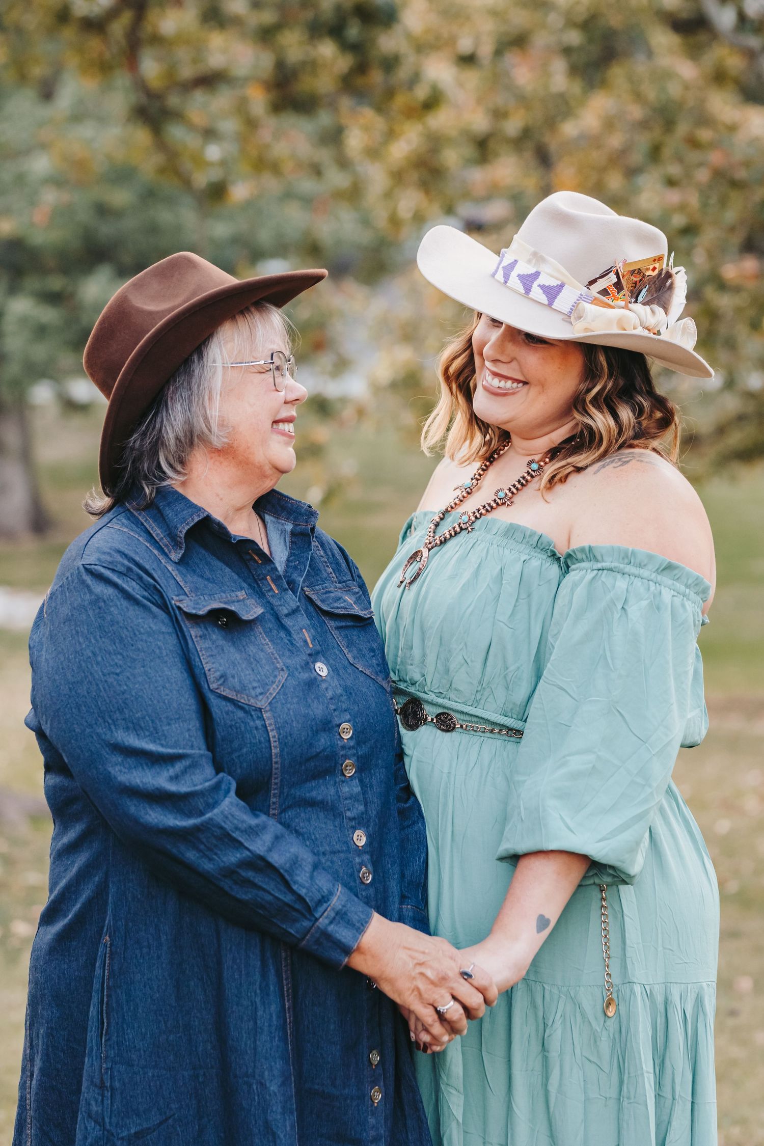 Two people in matching western hats share a joyful moment outdoors, wearing a denim dress and mint green dress.