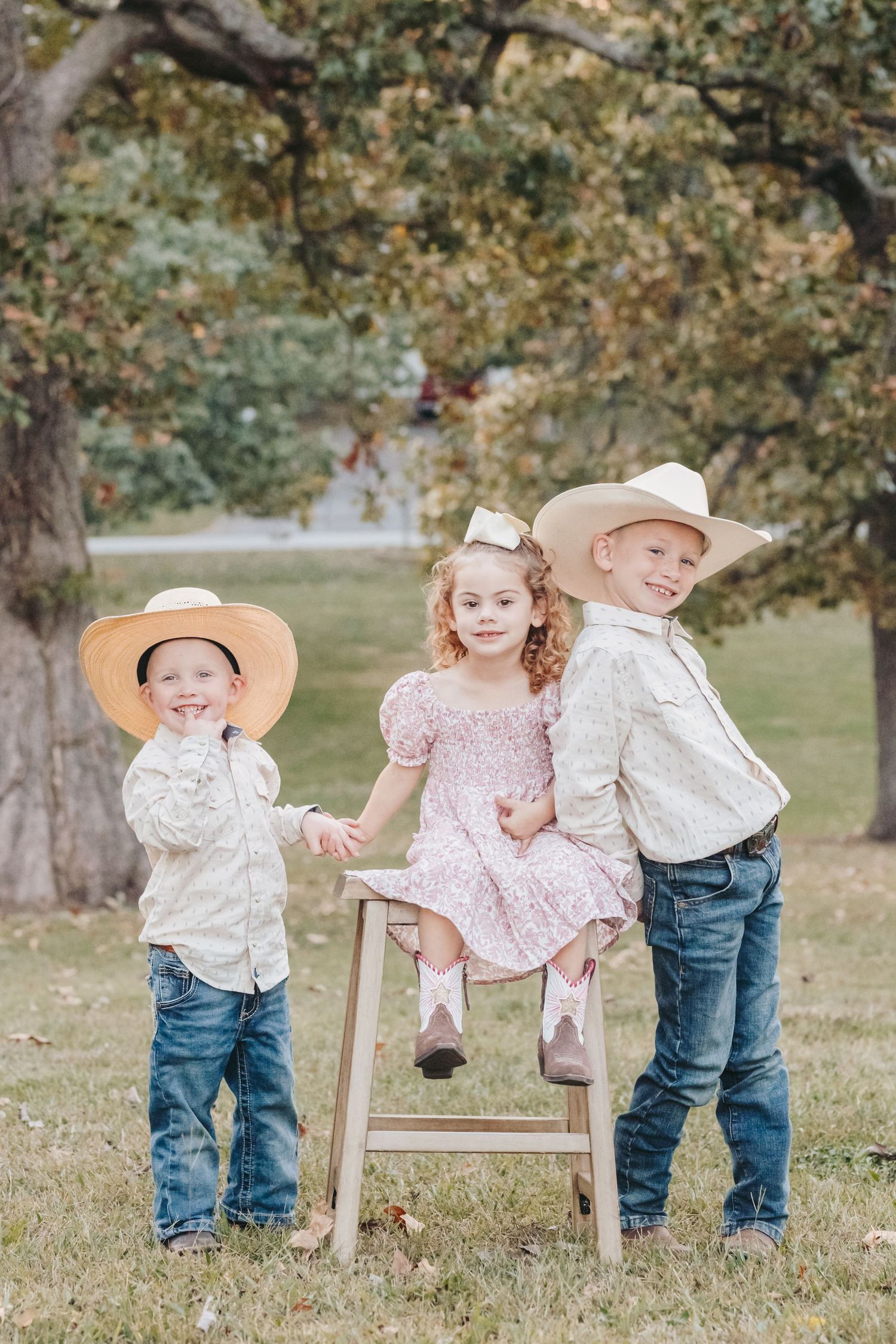 Children in western wear pose on a wooden step stool under autumn trees.