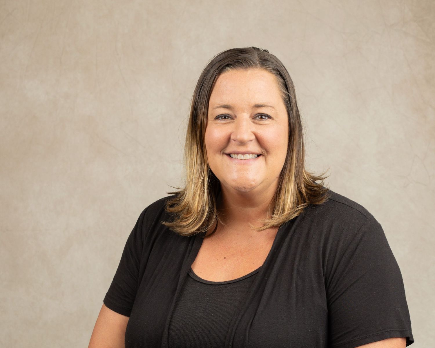 Professional studio portrait of a person in black clothing with a warm smile.