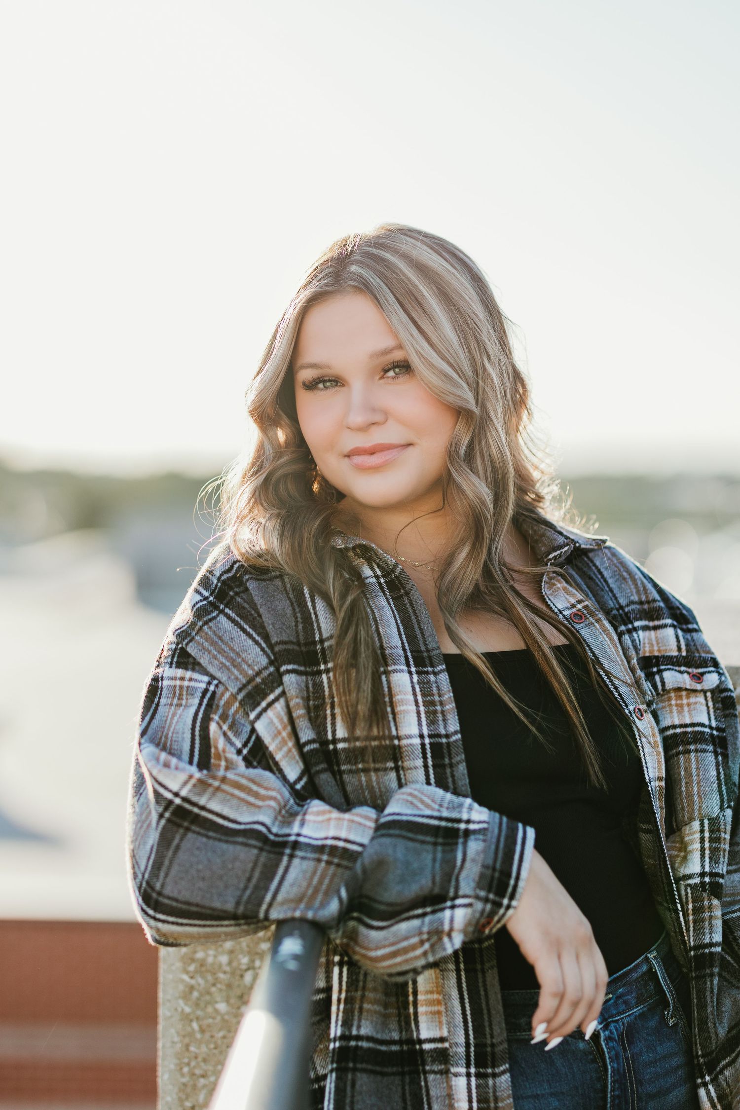 Woman in plaid flannel jacket poses outdoors during golden hour.