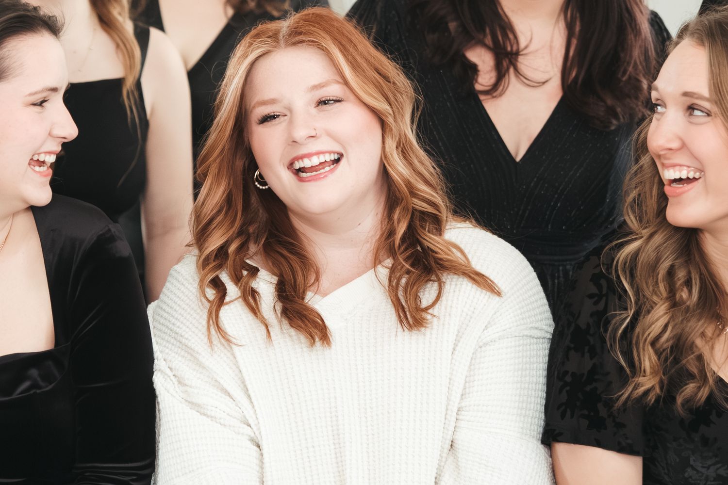 Three friends laugh together while wearing black and white outfits.
