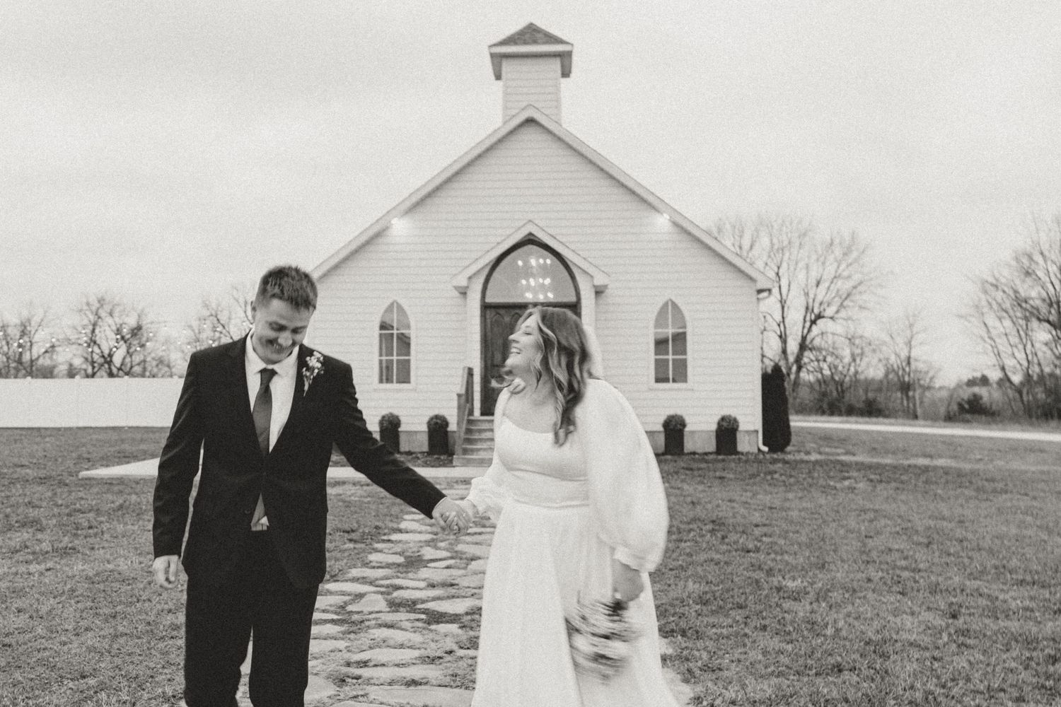 Black and white photo of newlyweds walking outside a classic white country church.