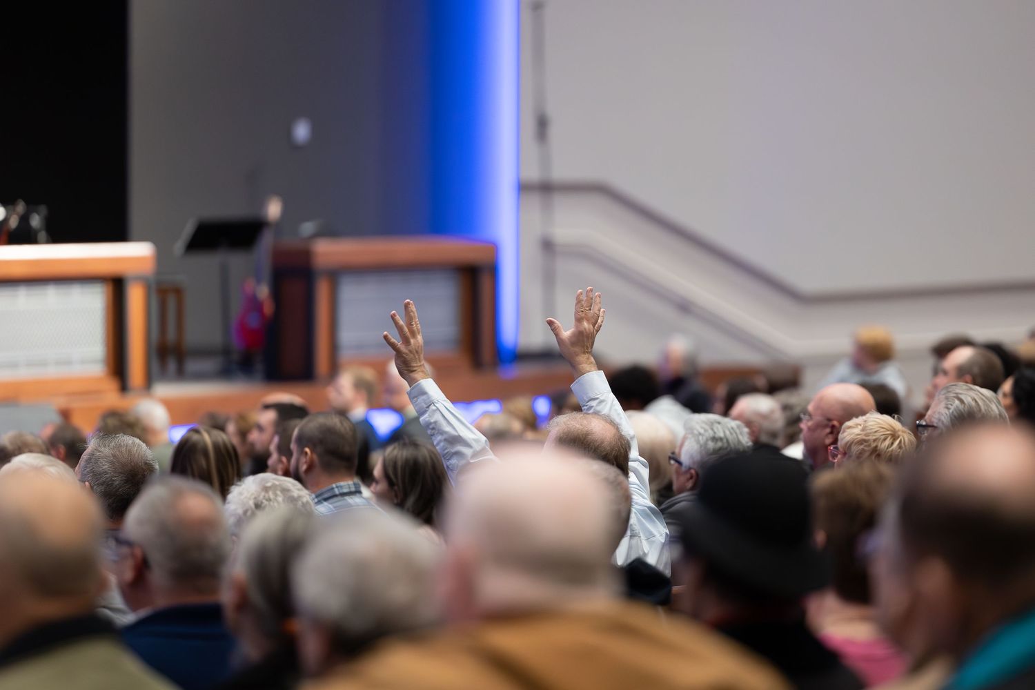 Raised hands visible among a crowded audience during what appears to be a church or conference gathering.