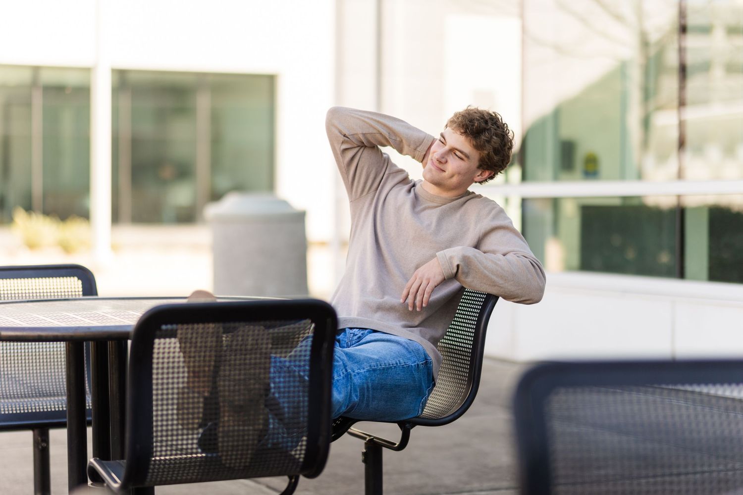 Person in gray sweater stretches and relaxes while sitting at outdoor patio table.