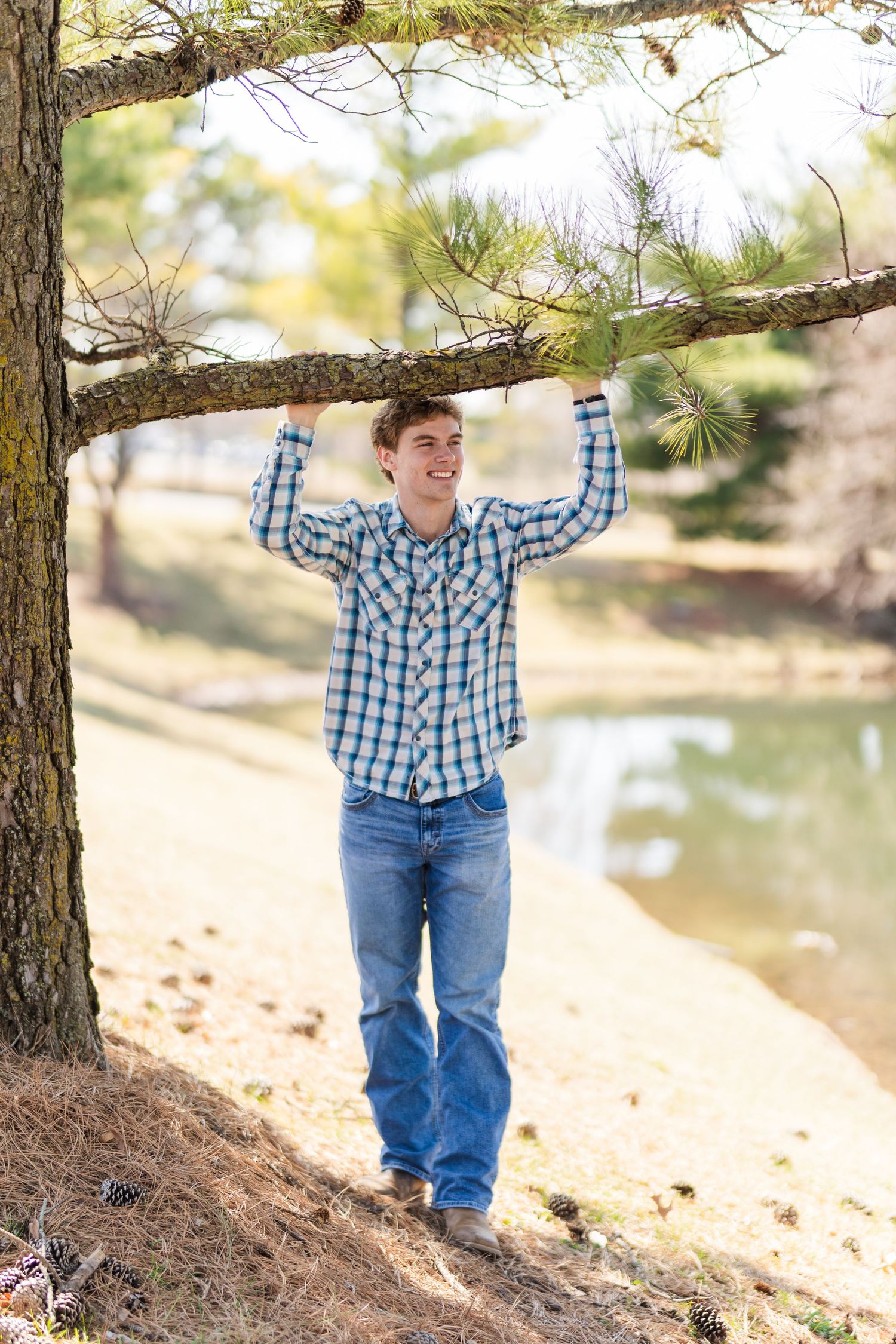 Person playfully poses holding tree branch by lake on sunny afternoon.