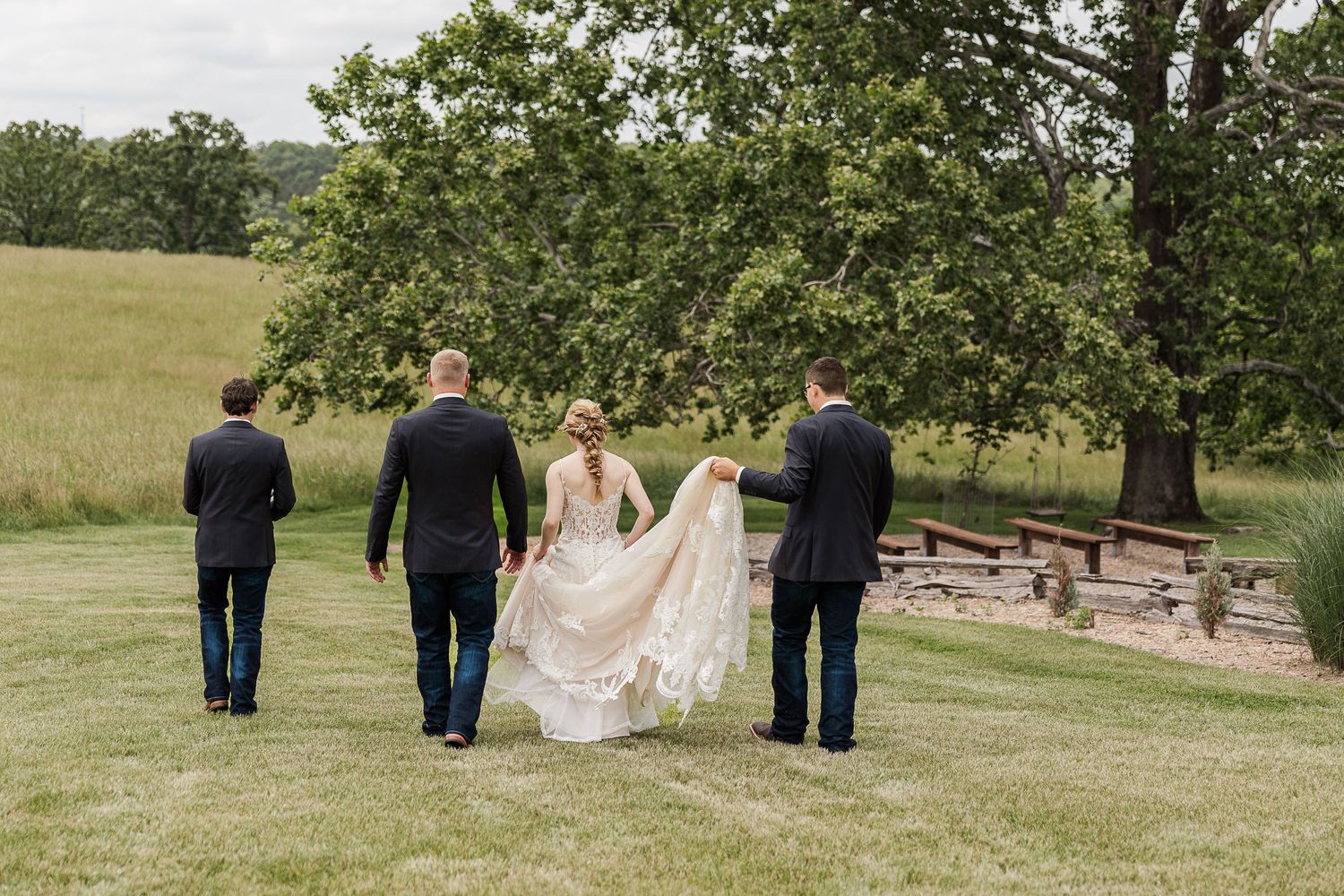 Formal group walking together on grassy hillside at outdoor wedding ceremony with stone steps in background.