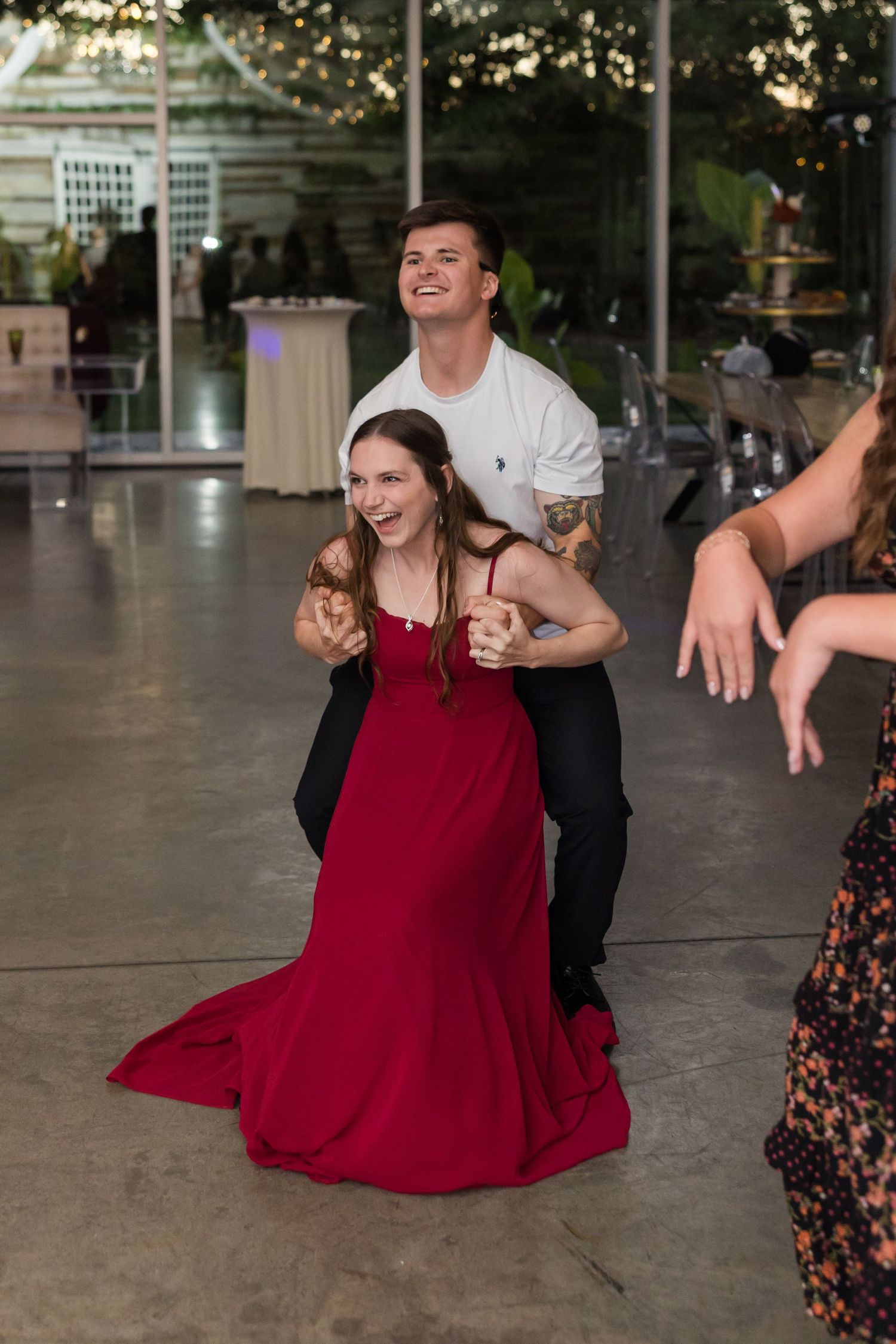 Wedding guest in red gown laughs joyfully while dancing with a partner at the reception.