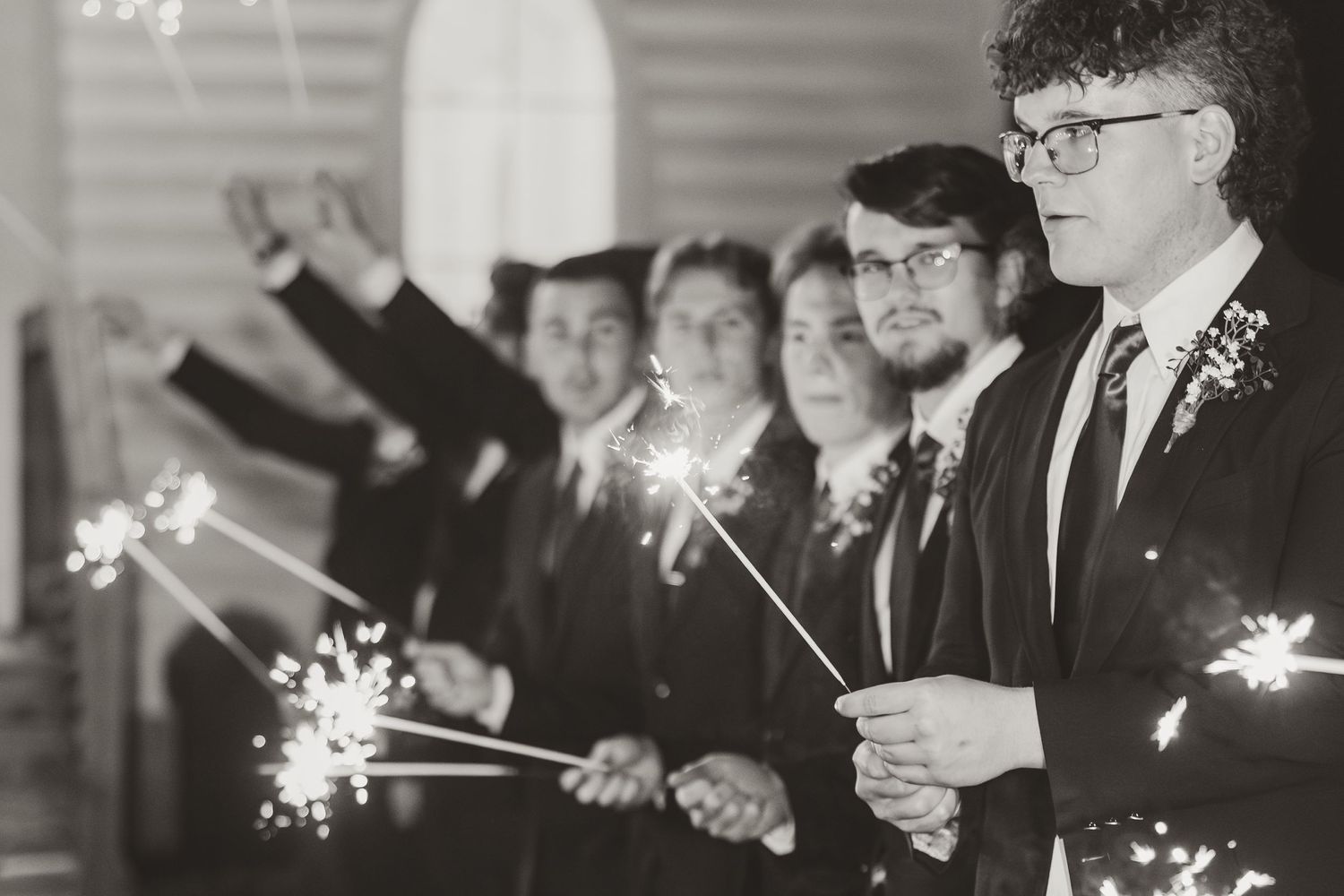 Wedding party members hold lit sparklers during evening celebration.