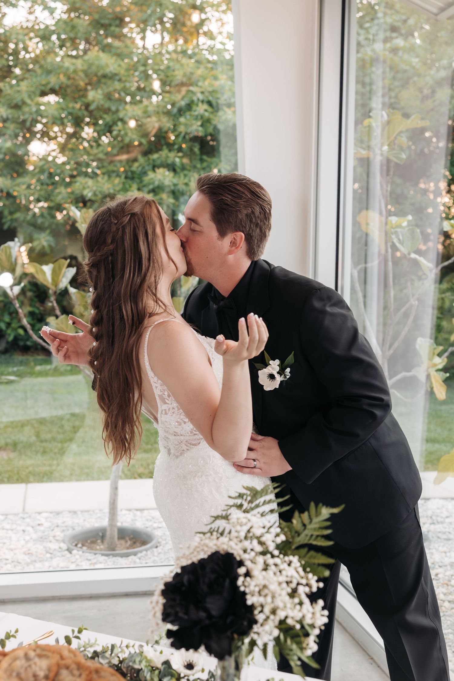 Newlyweds share their first kiss in a beautifully decorated reception venue with floral arrangements.