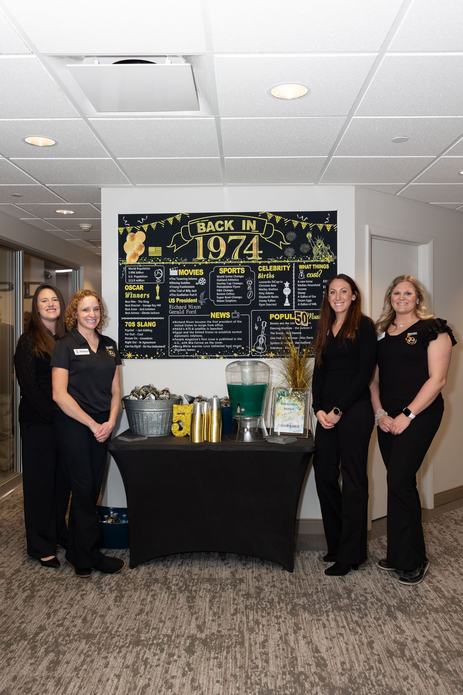 Staff members stand beside a 1974 themed display table with decorative chalkboard and refreshments.