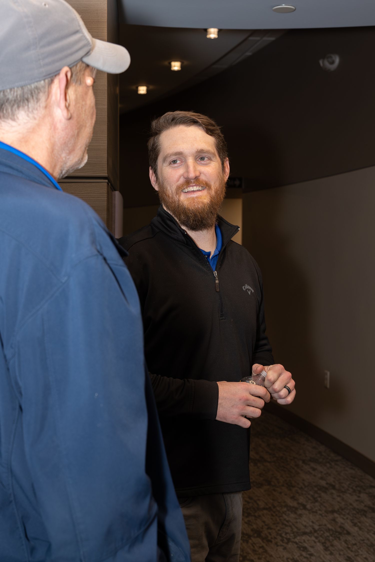 Two people having a conversation in a dimly lit office hallway.