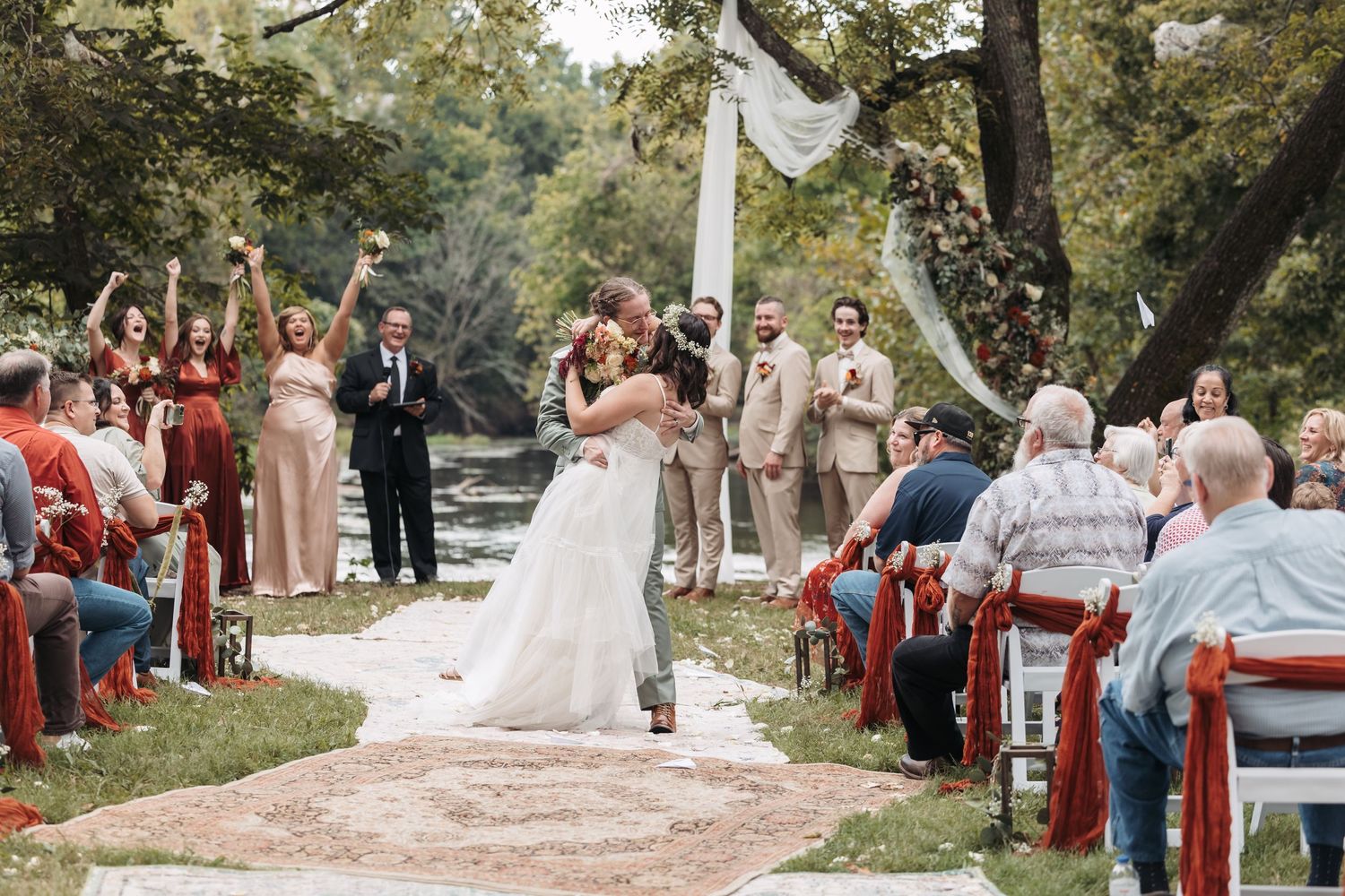 Outdoor wedding ceremony on tree-lined path with red chairs.
