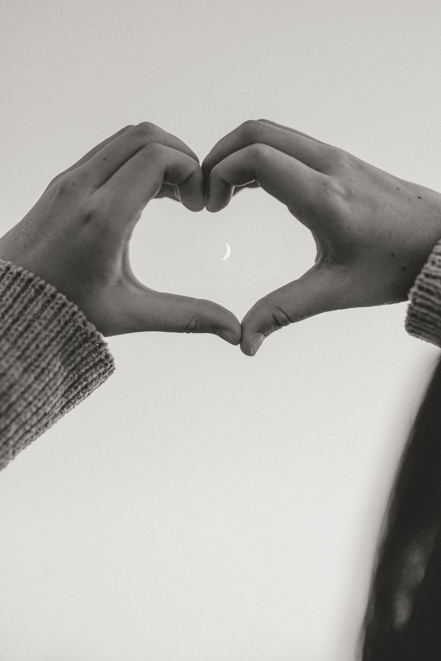 Hands forming heart shape against bright background in black and white photography.