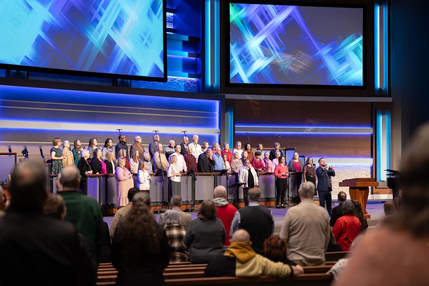 Large choir performing on stage with blue geometric backdrop displays.