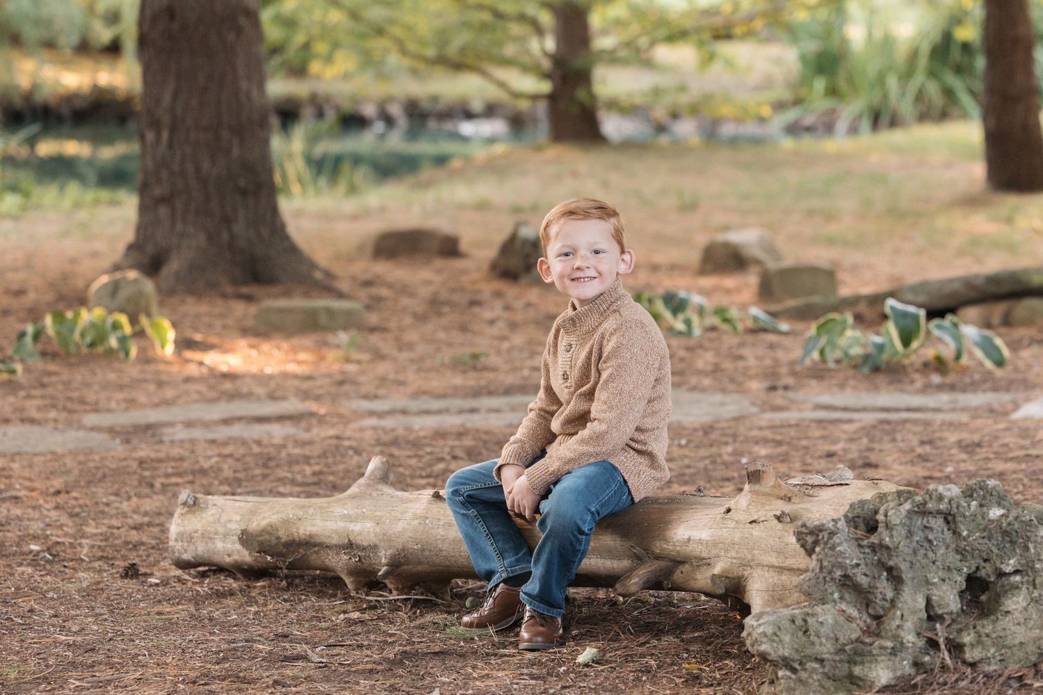 A small child sits on a fallen log in a wooded outdoor setting during autumn.