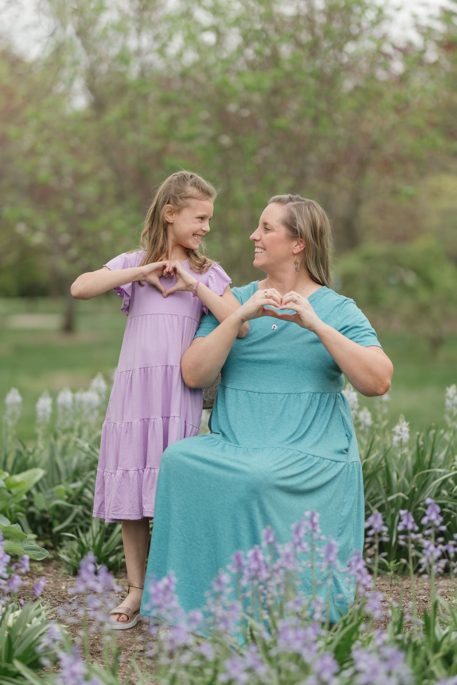 A mother and daughter make heart shapes with their hands in a blooming spring garden.