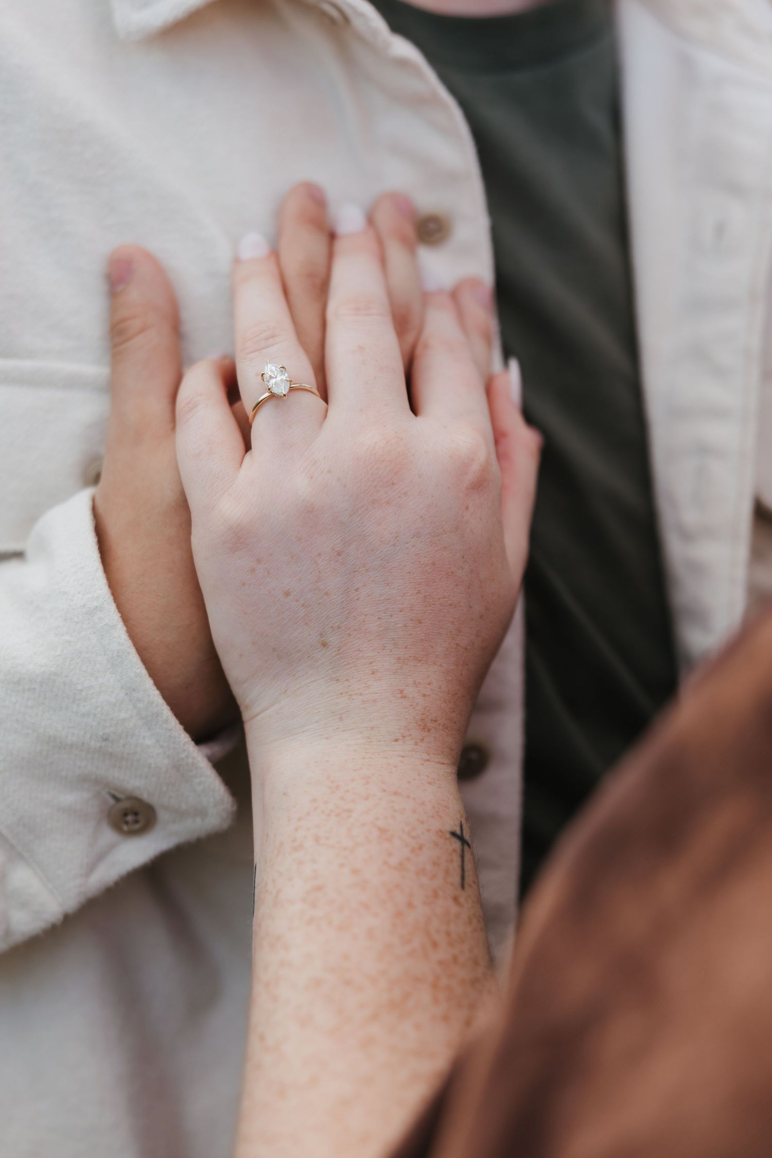 Close-up of hands showing engagement ring with cross tattoo detail.