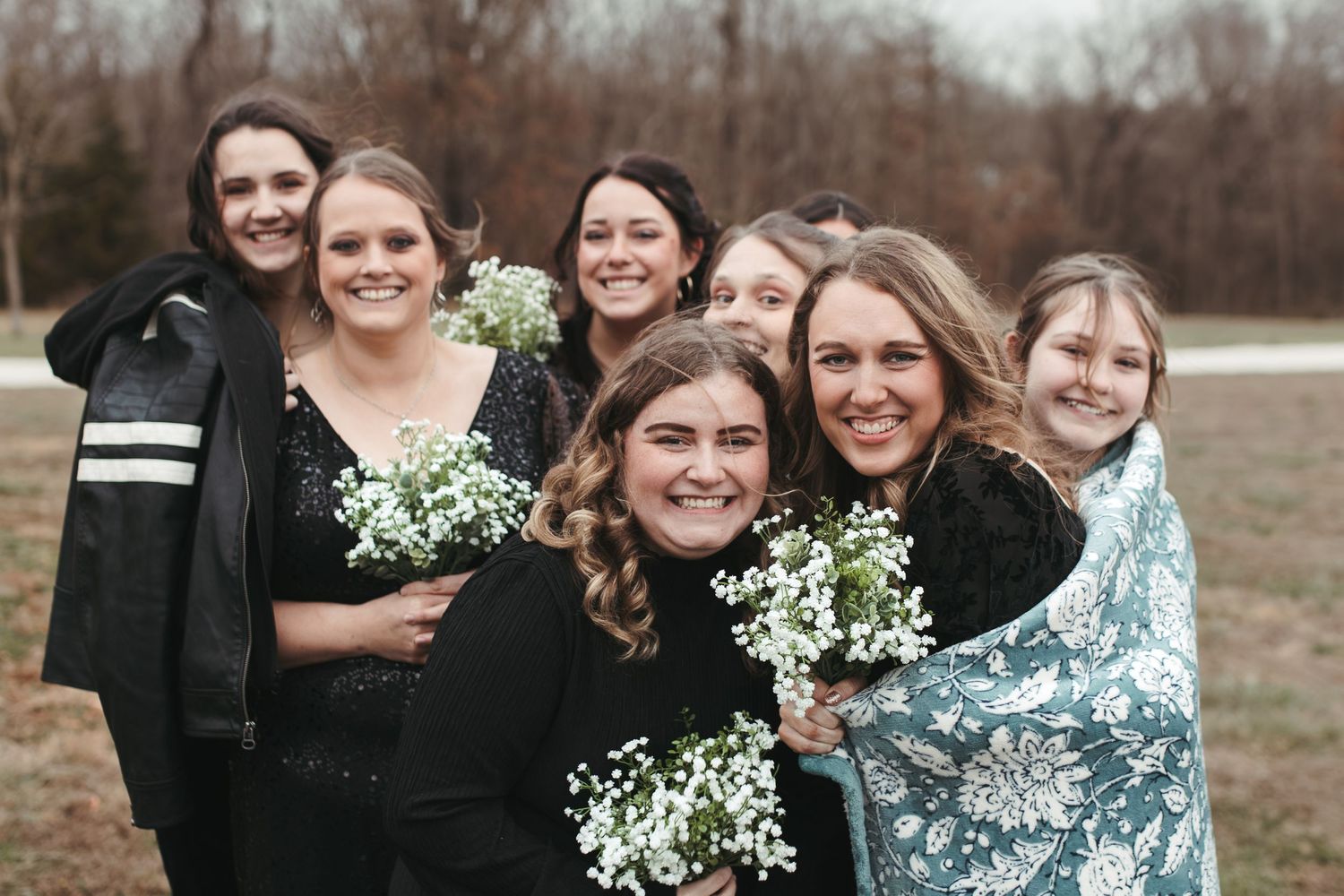 Bridesmaids in dark dresses hold white baby's breath bouquets while posing together outdoors.