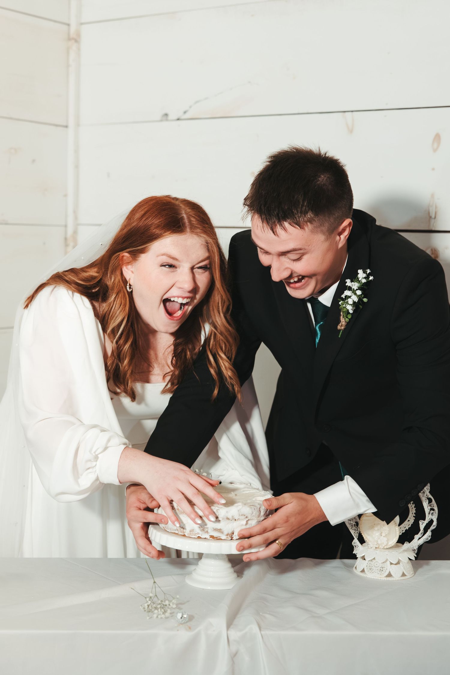 Couple laughs together while serving their wedding cake at reception.