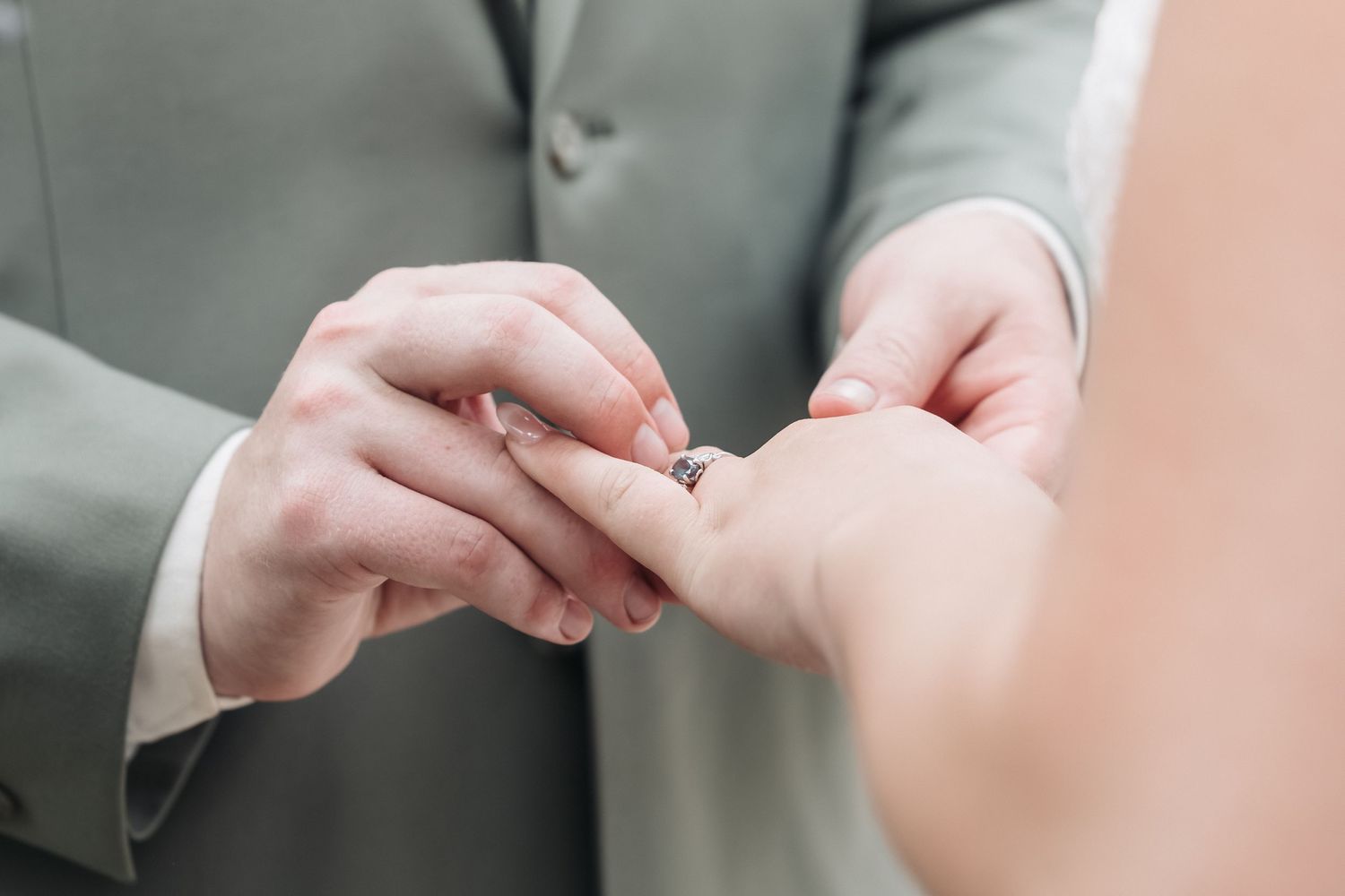 Close-up shot of hands exchanging wedding rings during ceremony.