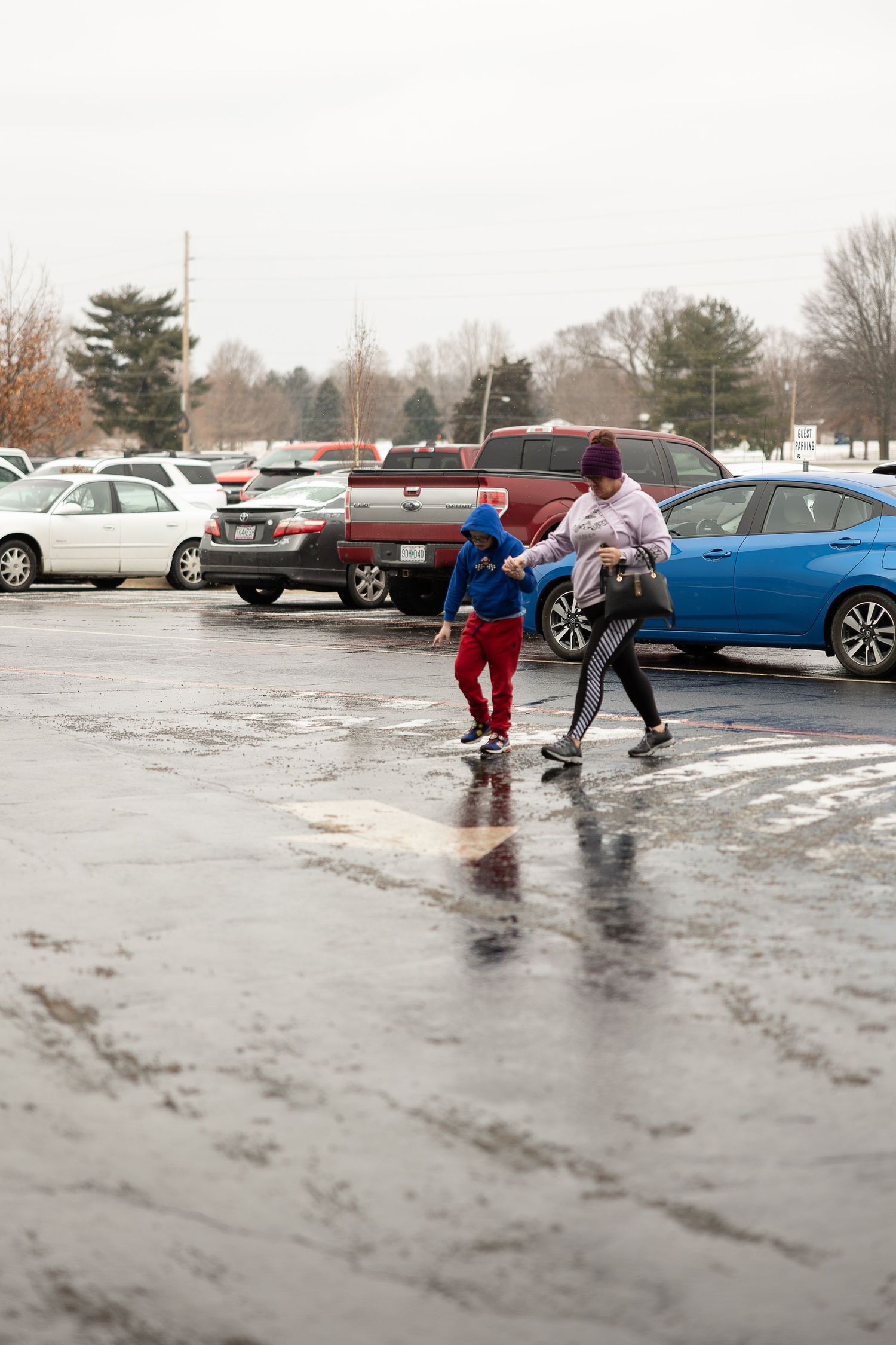 Two people walking through a wet parking lot on a rainy day.