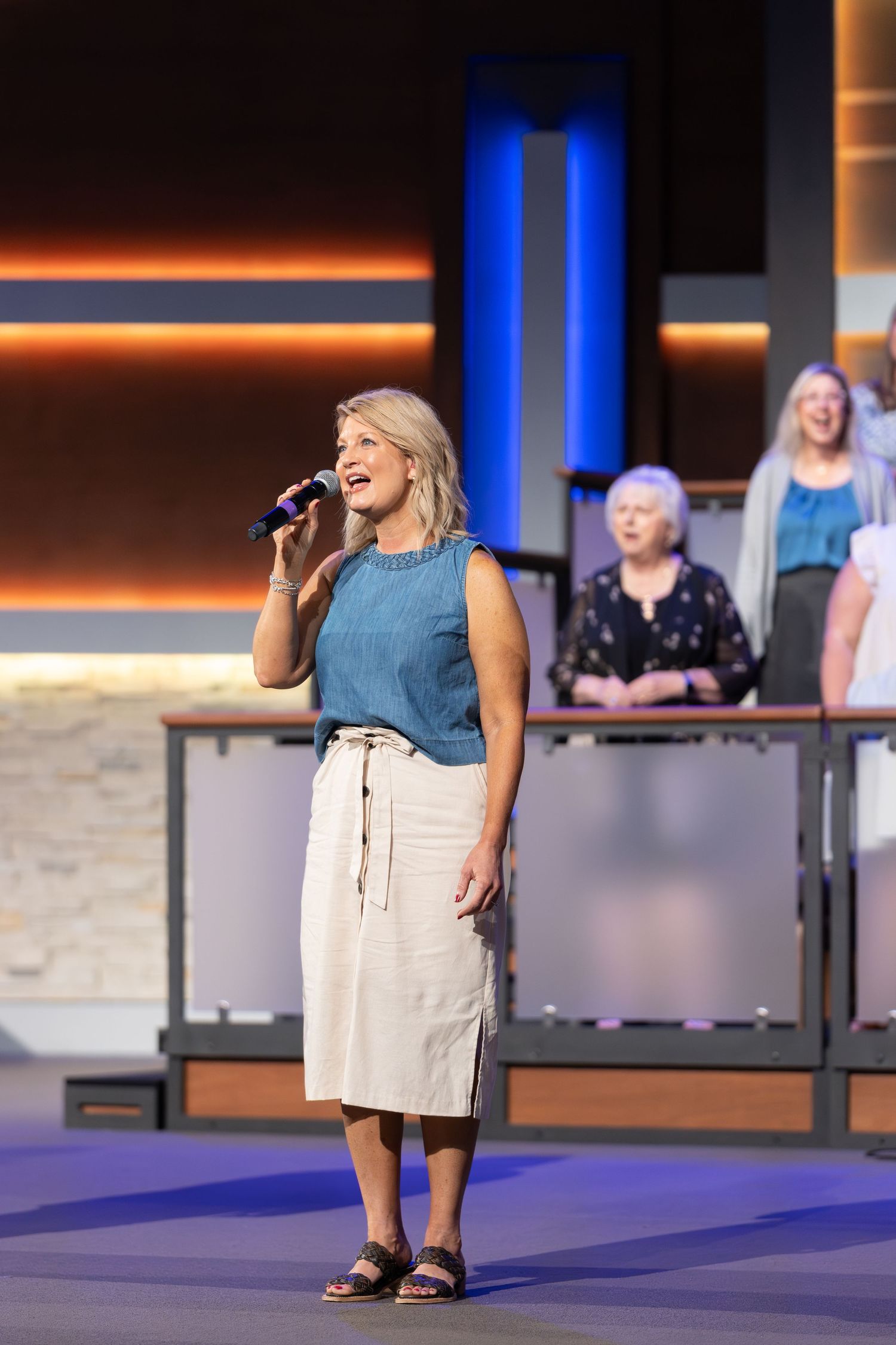 A performer sings on stage during a church service with contemporary decor and lighting.