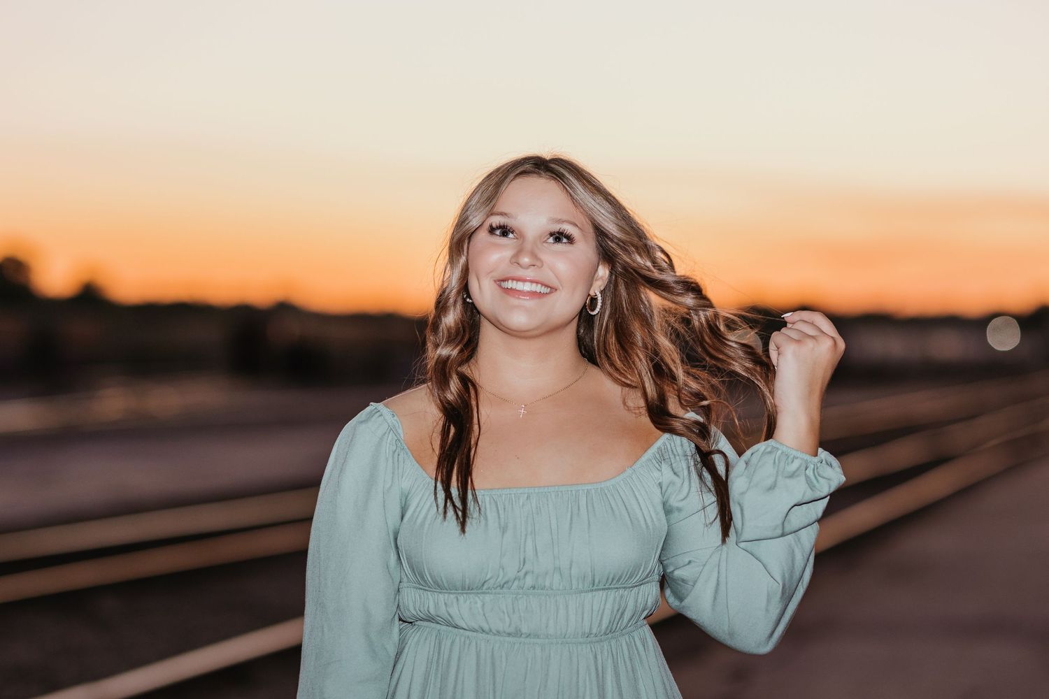 Person in sage dress poses outdoors during golden hour sunset.