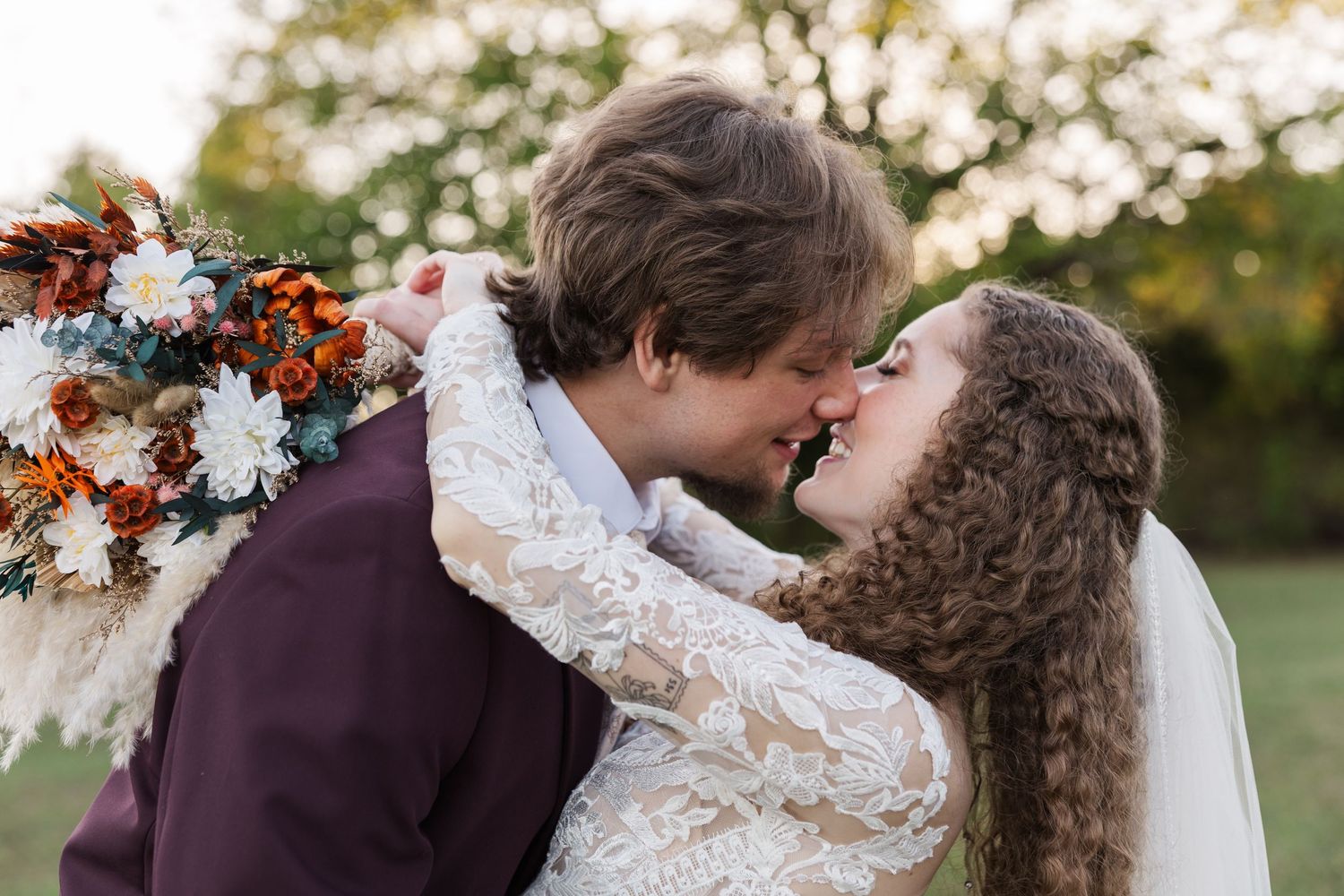 A romantic kiss between newlyweds surrounded by autumn flowers and natural outdoor scenery.