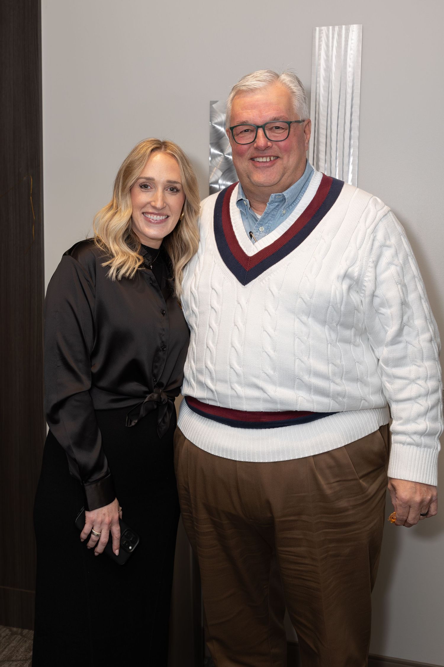 Professional photo of two people at an event, one wearing a white cable knit sweater.