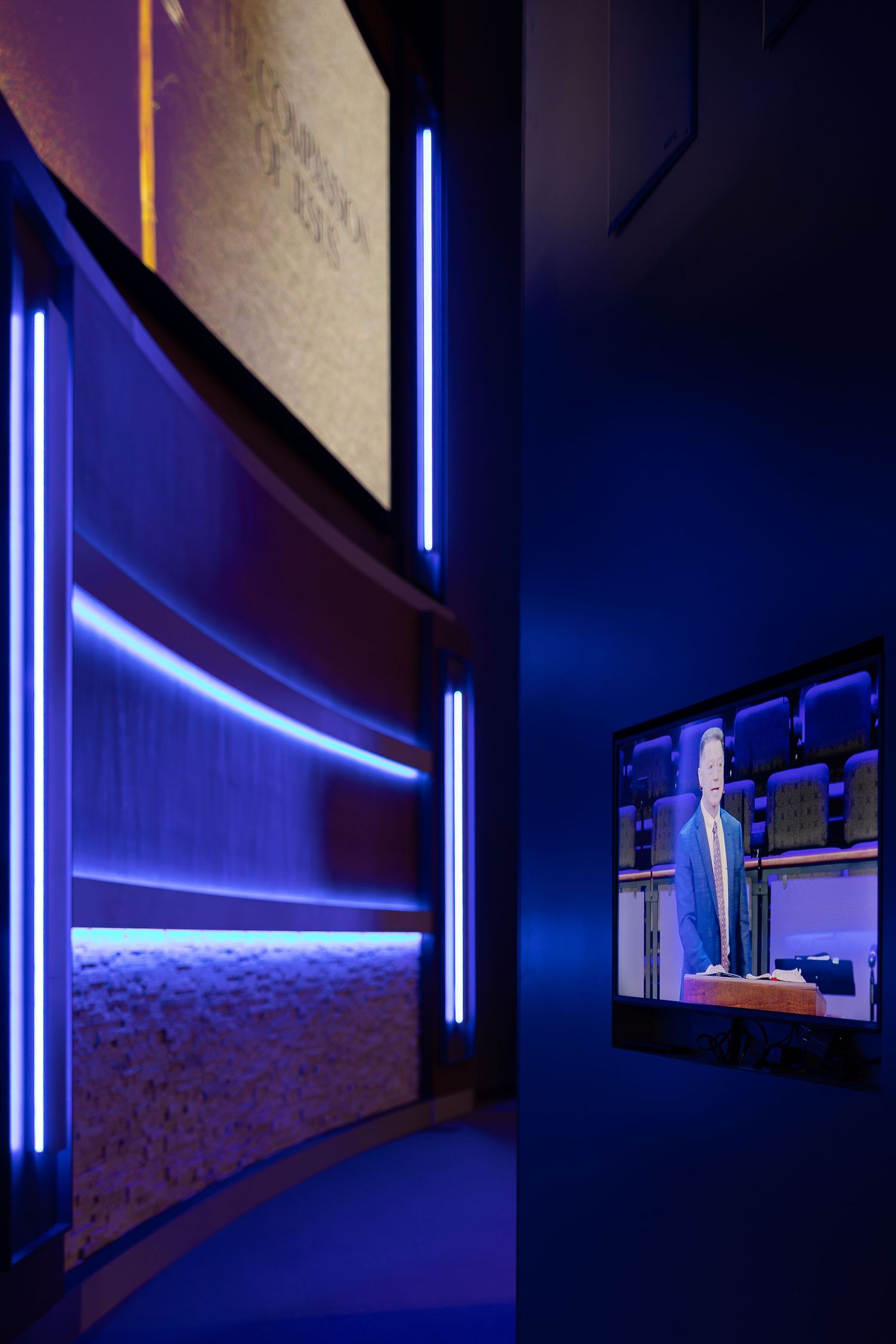 Modern hallway with curved walls featuring blue LED lighting strips and a video display screen.