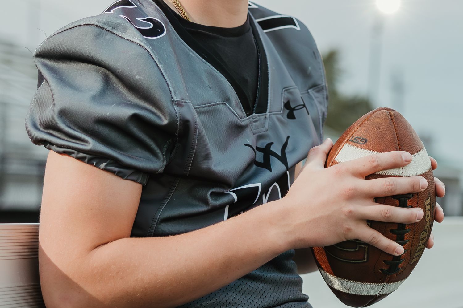 Close up of football player holding brown leather football in grey jersey.