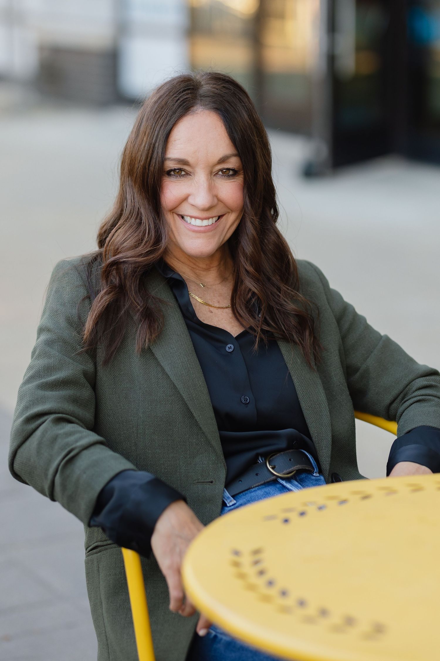 Relaxed business portrait in olive blazer at outdoor cafe with yellow table.