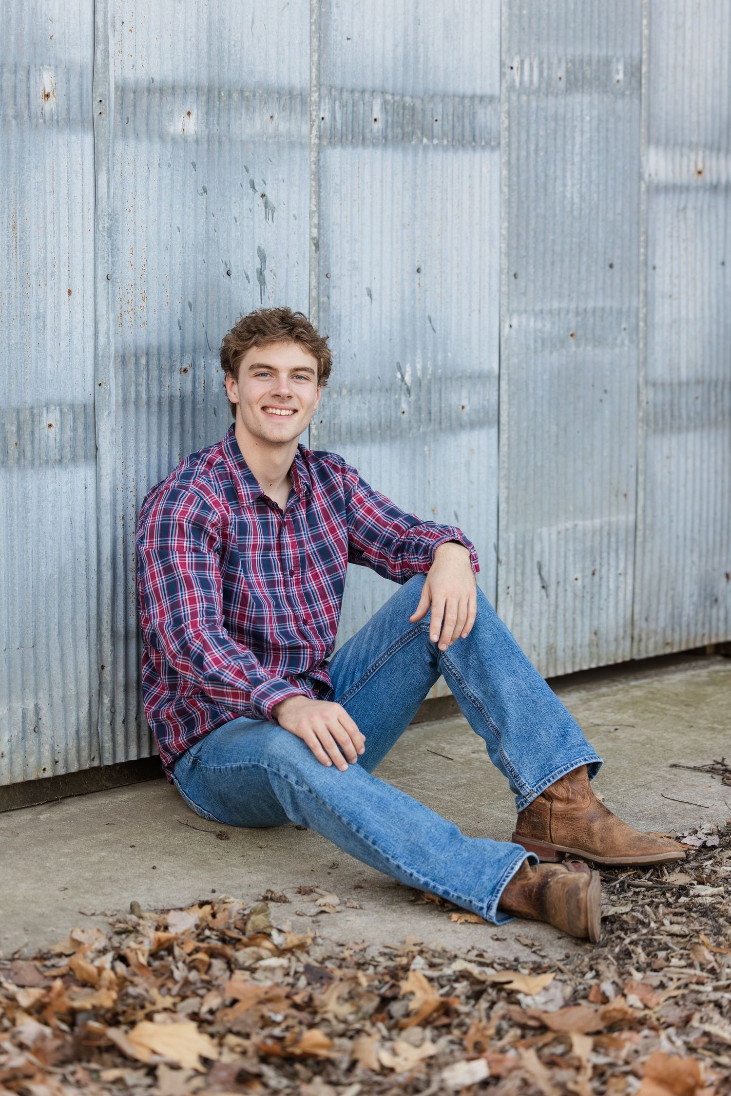 Casual portrait against corrugated metal wall with scattered autumn leaves on ground.