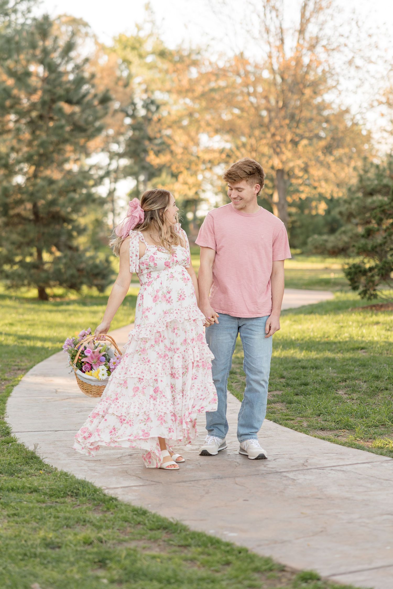 A couple walking and twirling on a concrete path surrounded by autumn trees and grass on a sunny afternoon.