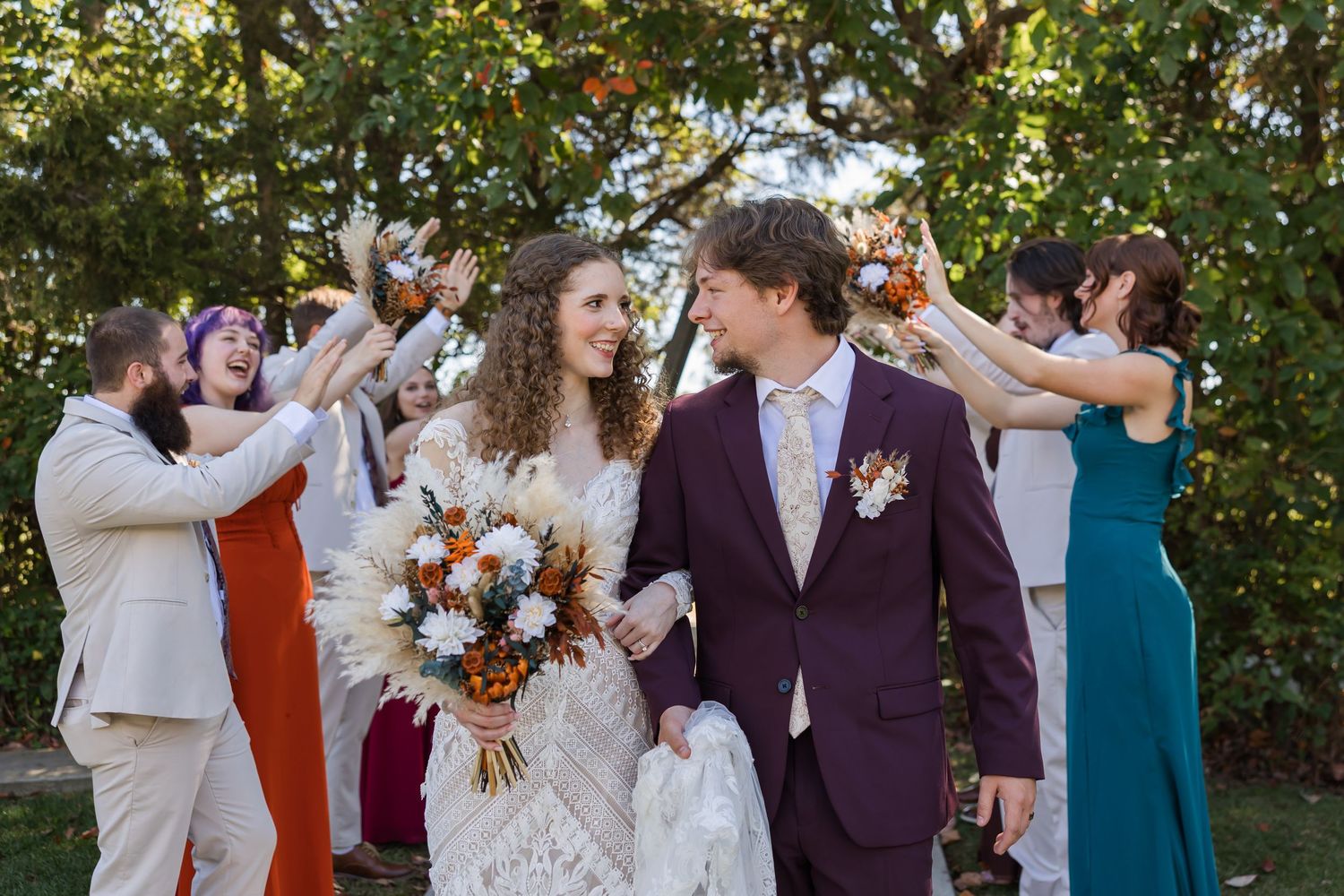 Wedding celebration outdoors with guests tossing flower petals as newlyweds walk together holding autumn-themed bouquet.