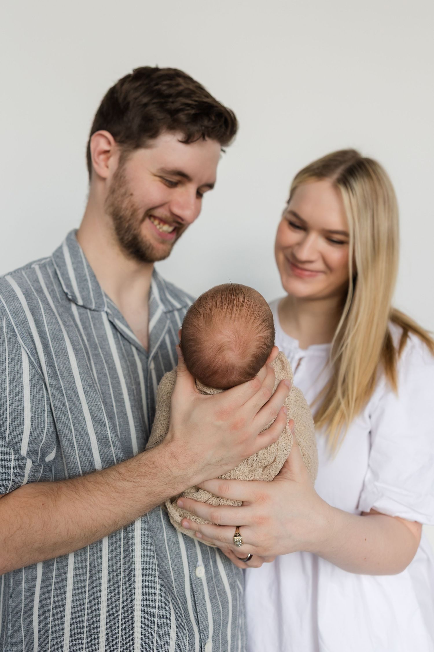 A loving family moment captured in sequence as parents share affectionate moments with their swaddled newborn.