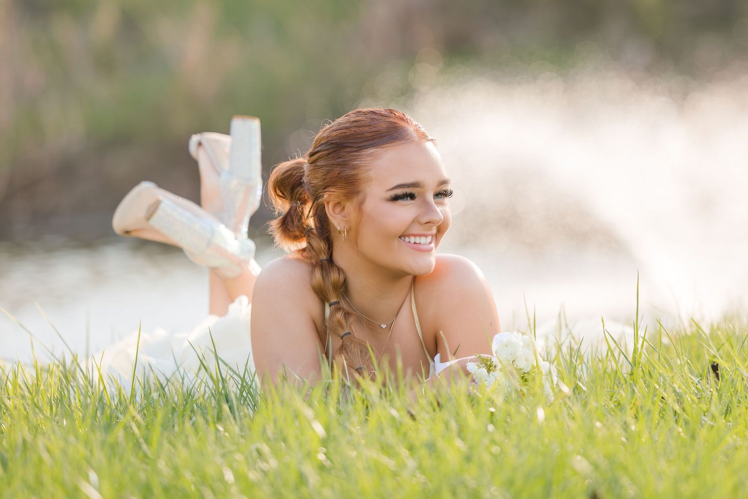 A young person in a sleeveless white top lays in the grass during a sunny outdoor photo session.