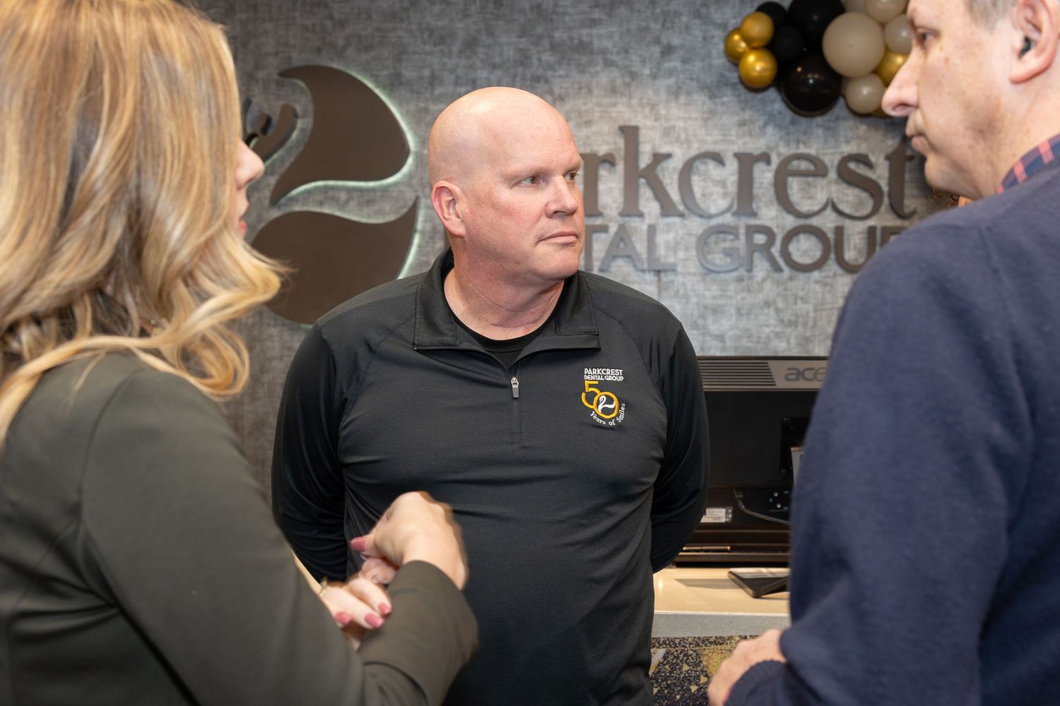 People conversing near a company logo wall in business attire.
