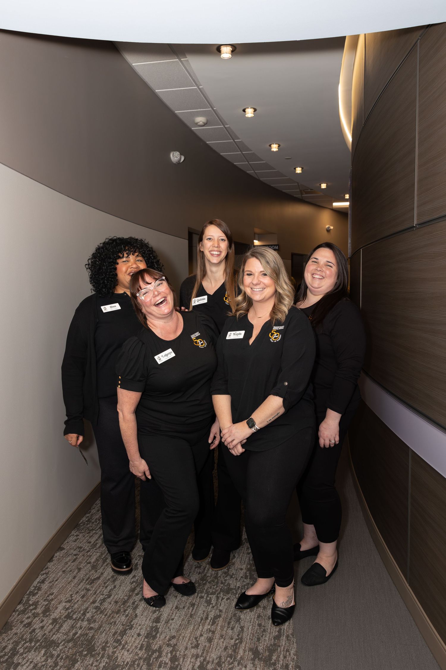 Team members in matching black attire pose together in an office hallway.