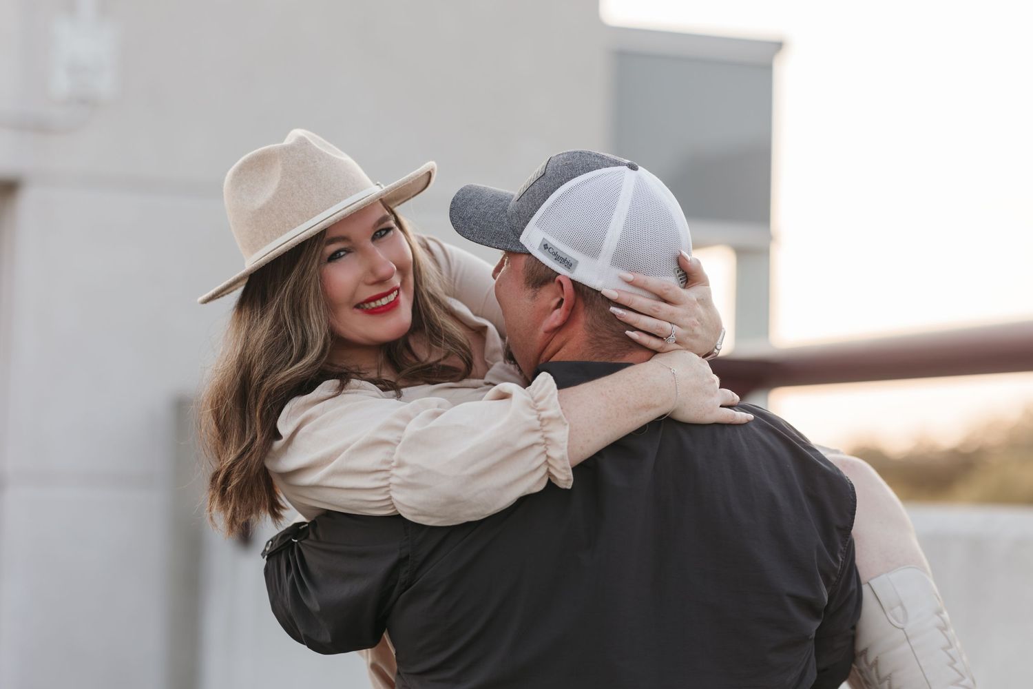 Romantic couple sharing a playful moment at sunset with woman in beige hat and man in baseball cap embracing.